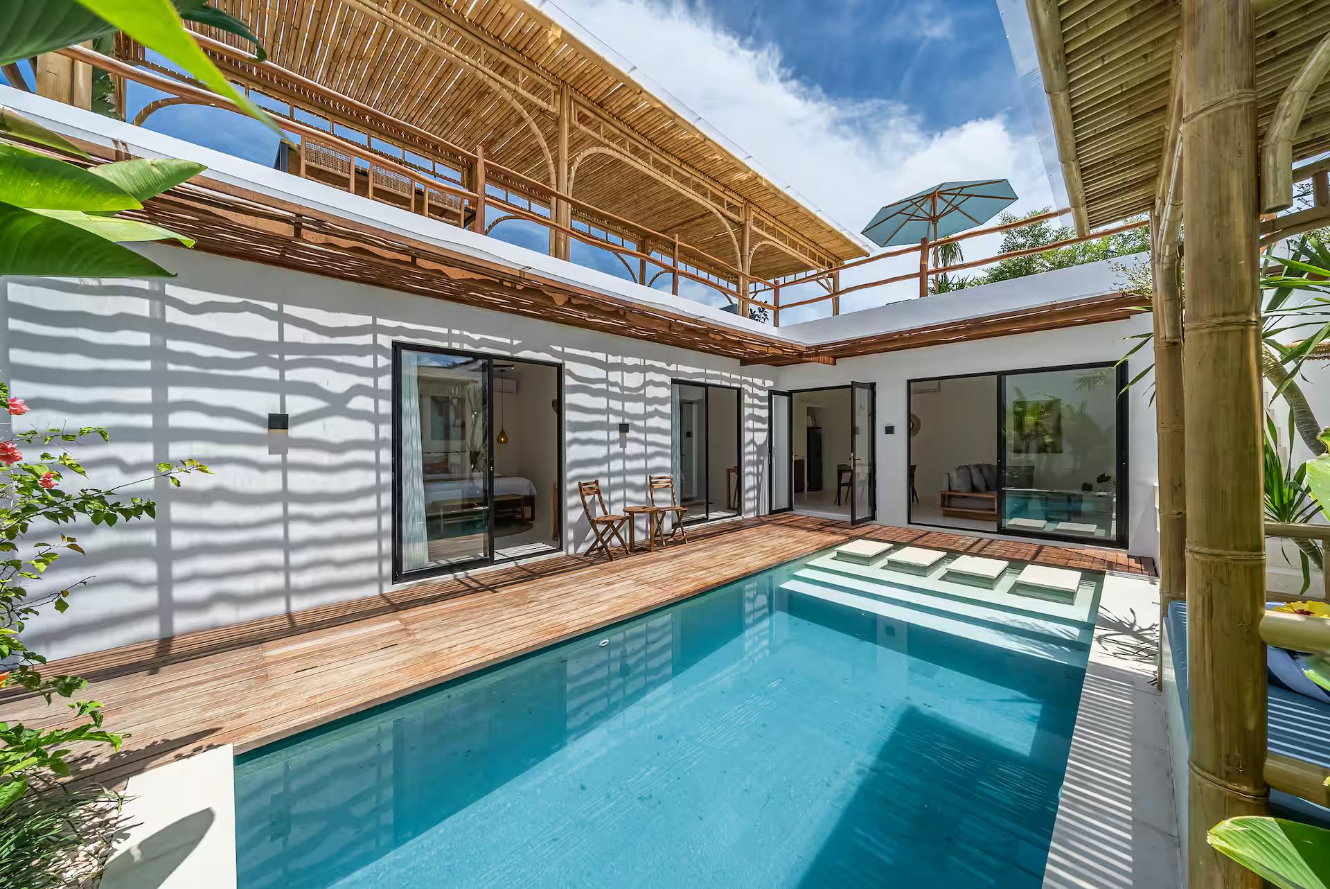 The long pool at Villa Dara running beside its timber deck, ribbed white walls and bamboo roof above
