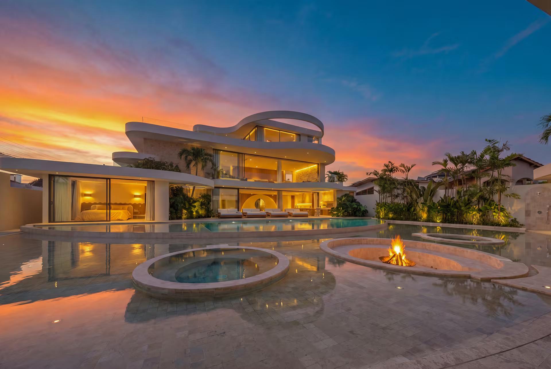Villa Babylon at sunset, its curved roof planes lit above a pool ringed around a sunken fire pit