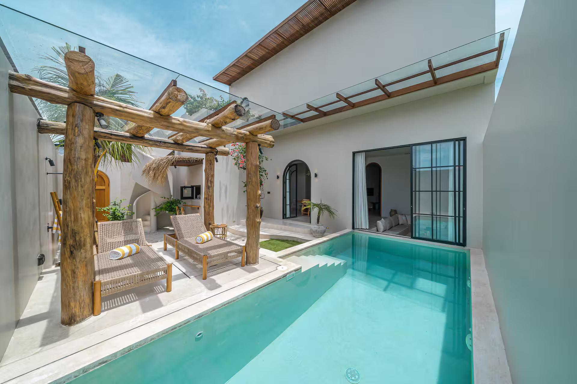 A turquoise lap pool at Casa 24 beneath a pergola of rough timber posts, teak loungers alongside