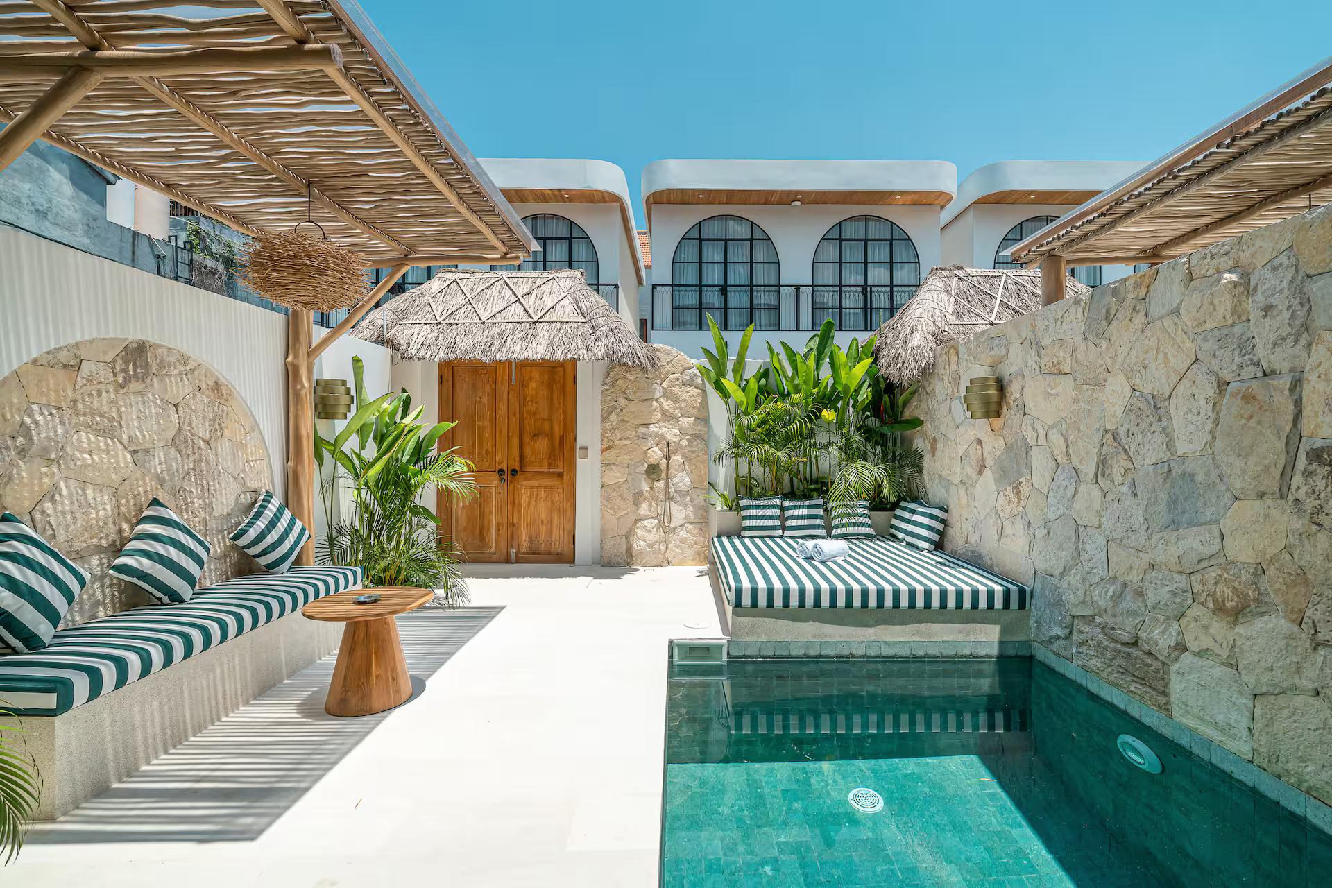 The green-tiled plunge pool at Villa Arnie, stone walls and a thatched parasol above the bench