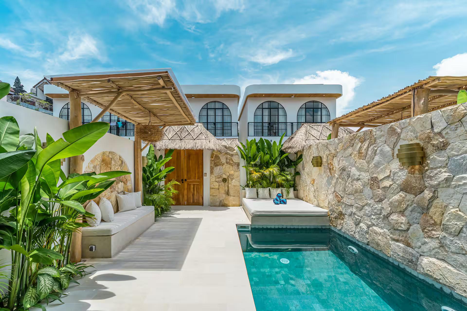 The courtyard pool at Villa Shams below a thatched pergola and rough limestone walls