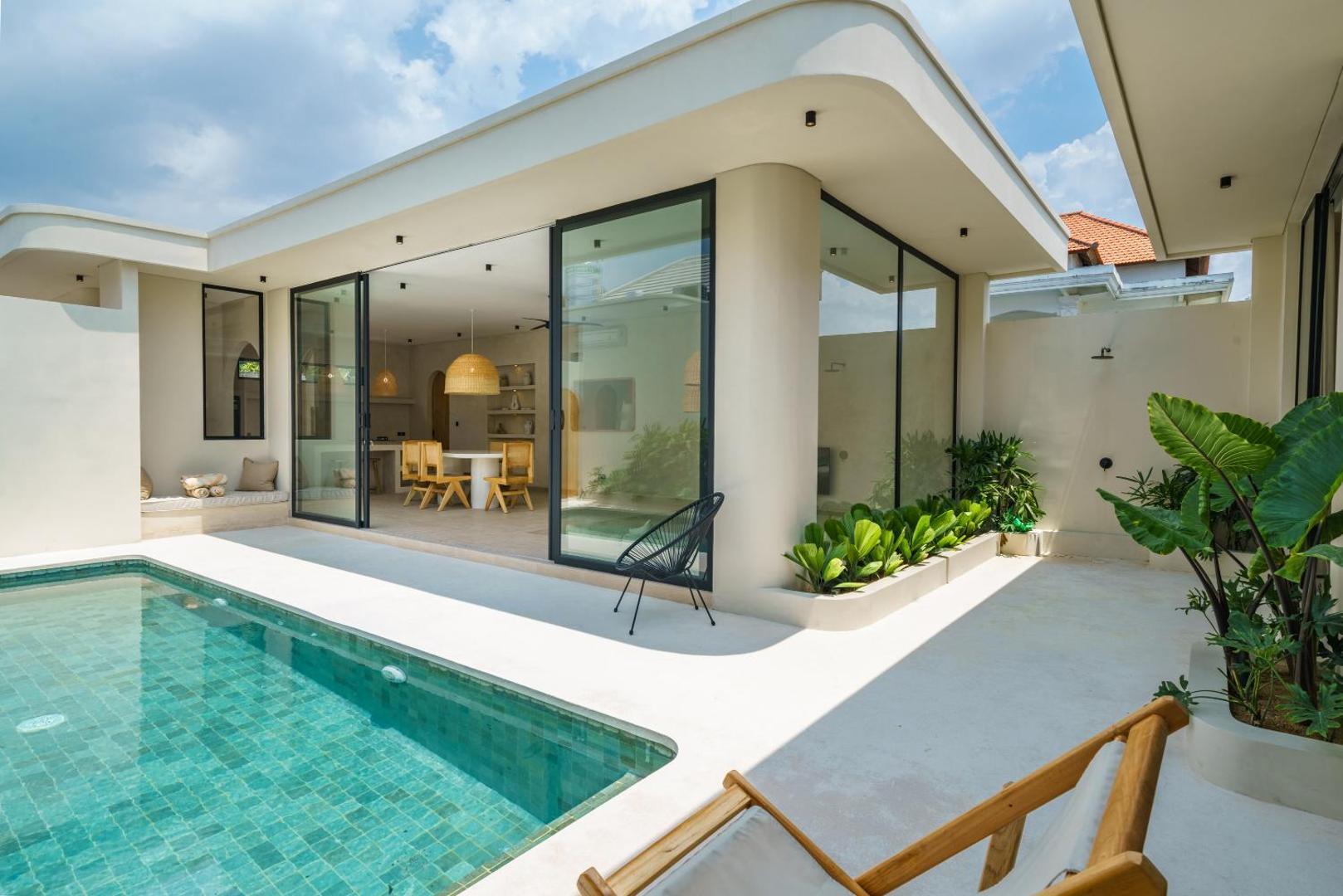 Glass doors folded open to the dining room, with a deck chair and planters beside the green-tiled pool