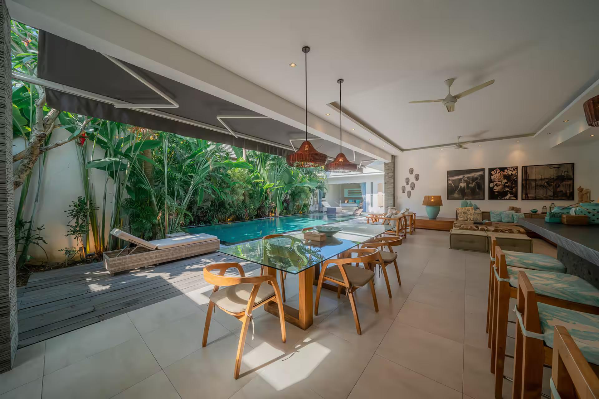 Dining table under a retractable awning at the pool edge, copper pendants overhead