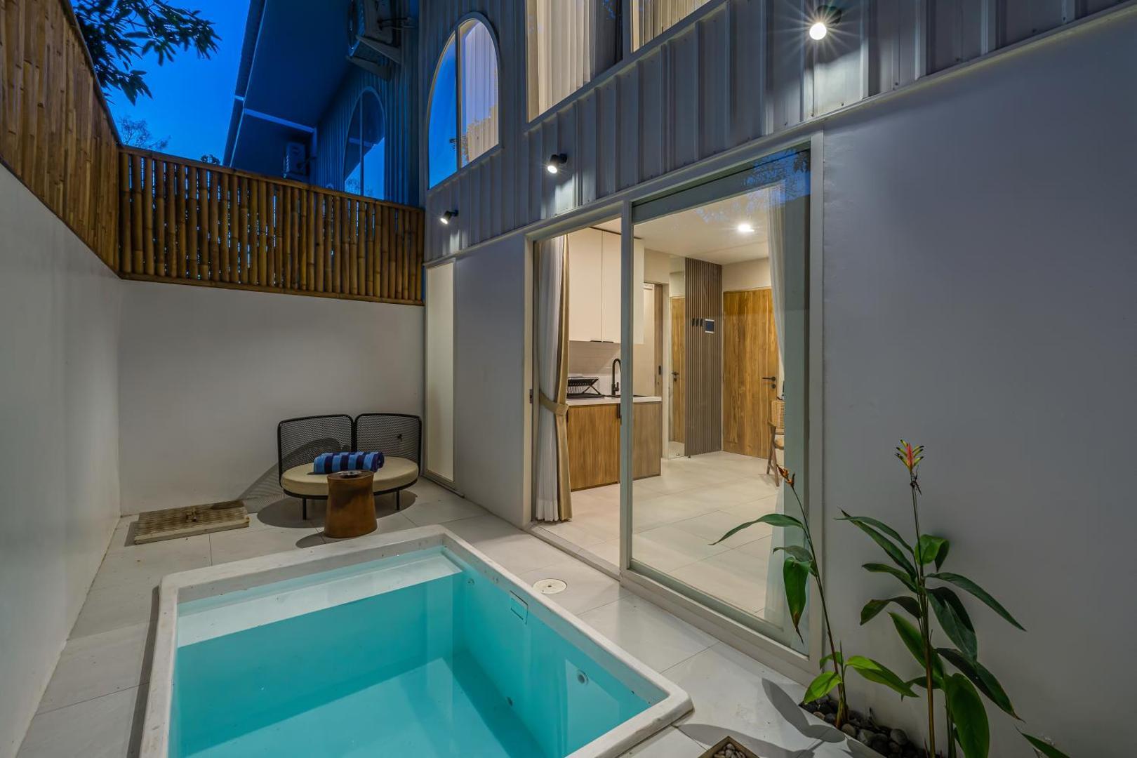 Dusk over the courtyard pool, the kitchenette lit behind sliding glass