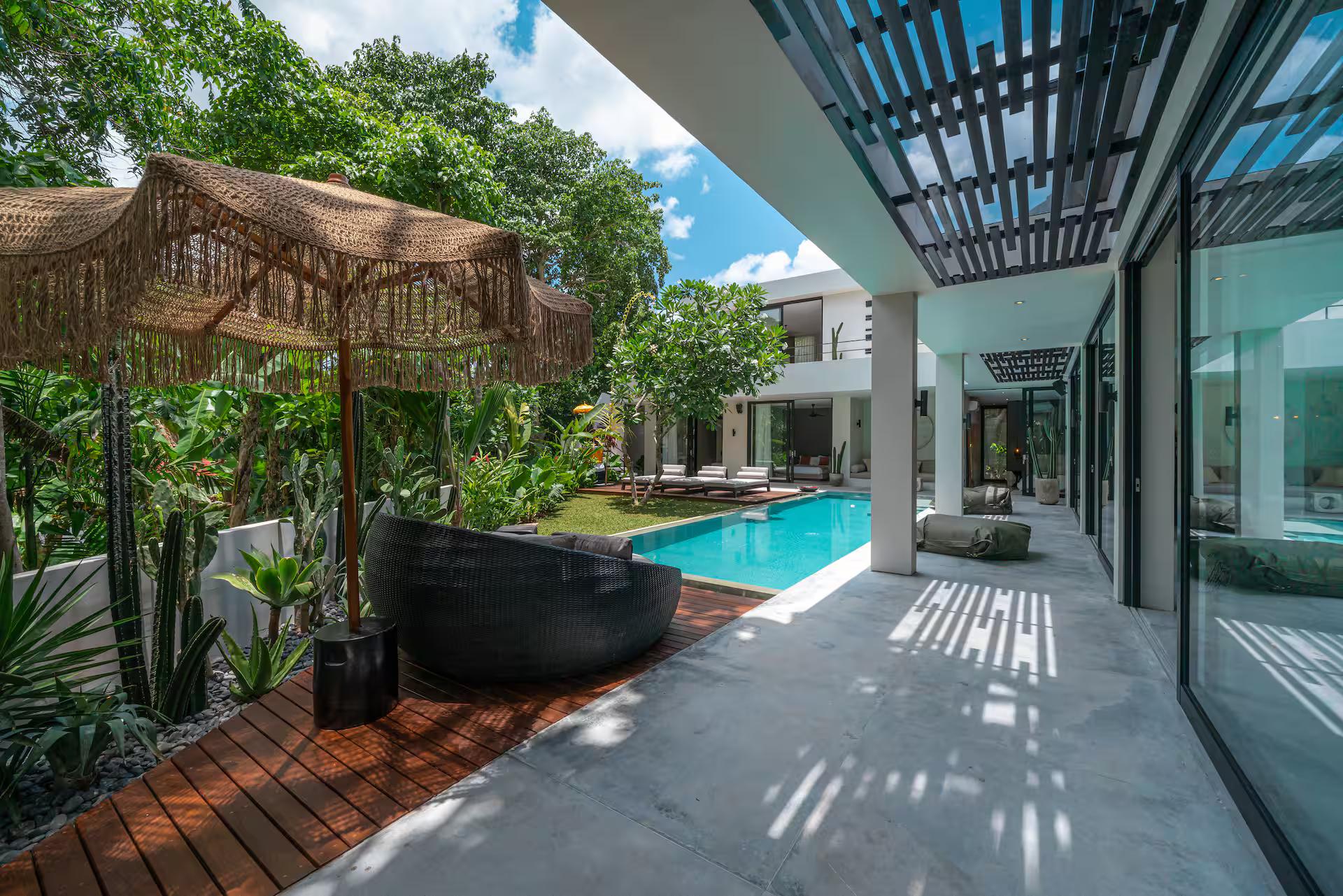 Black stone bath set in dark pebbles beside the pool walkway, thatched parasol overhead