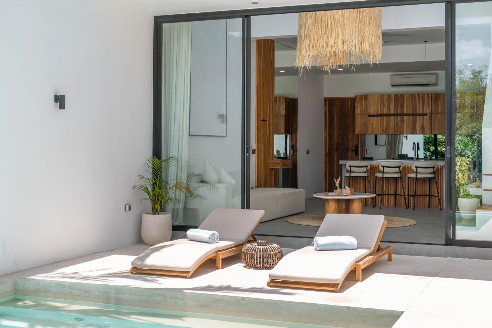 Two timber sun loungers beside the pool, the living room open behind sliding glass