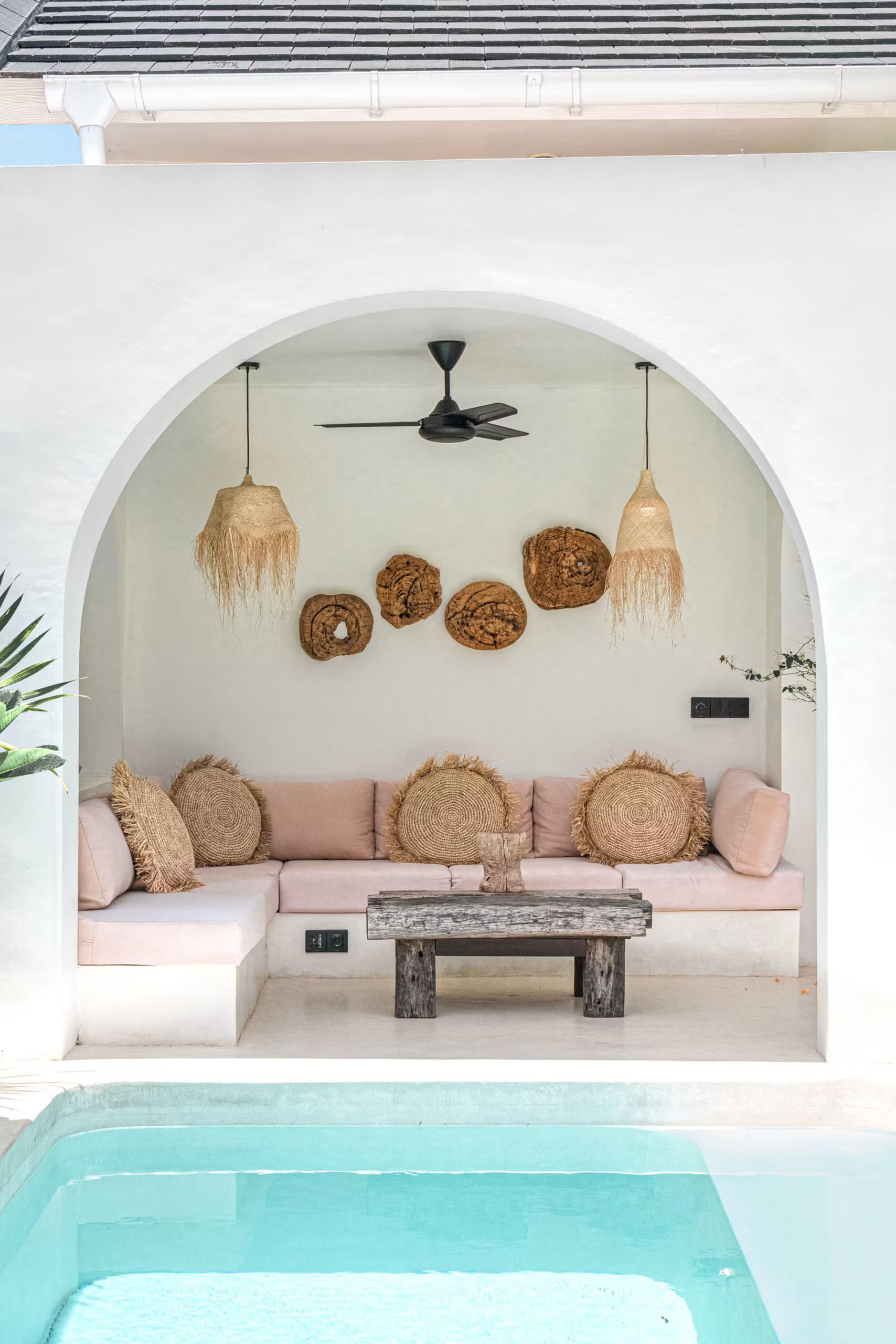 Arched poolside alcove with a blush cushioned banquette and a rustic timber table