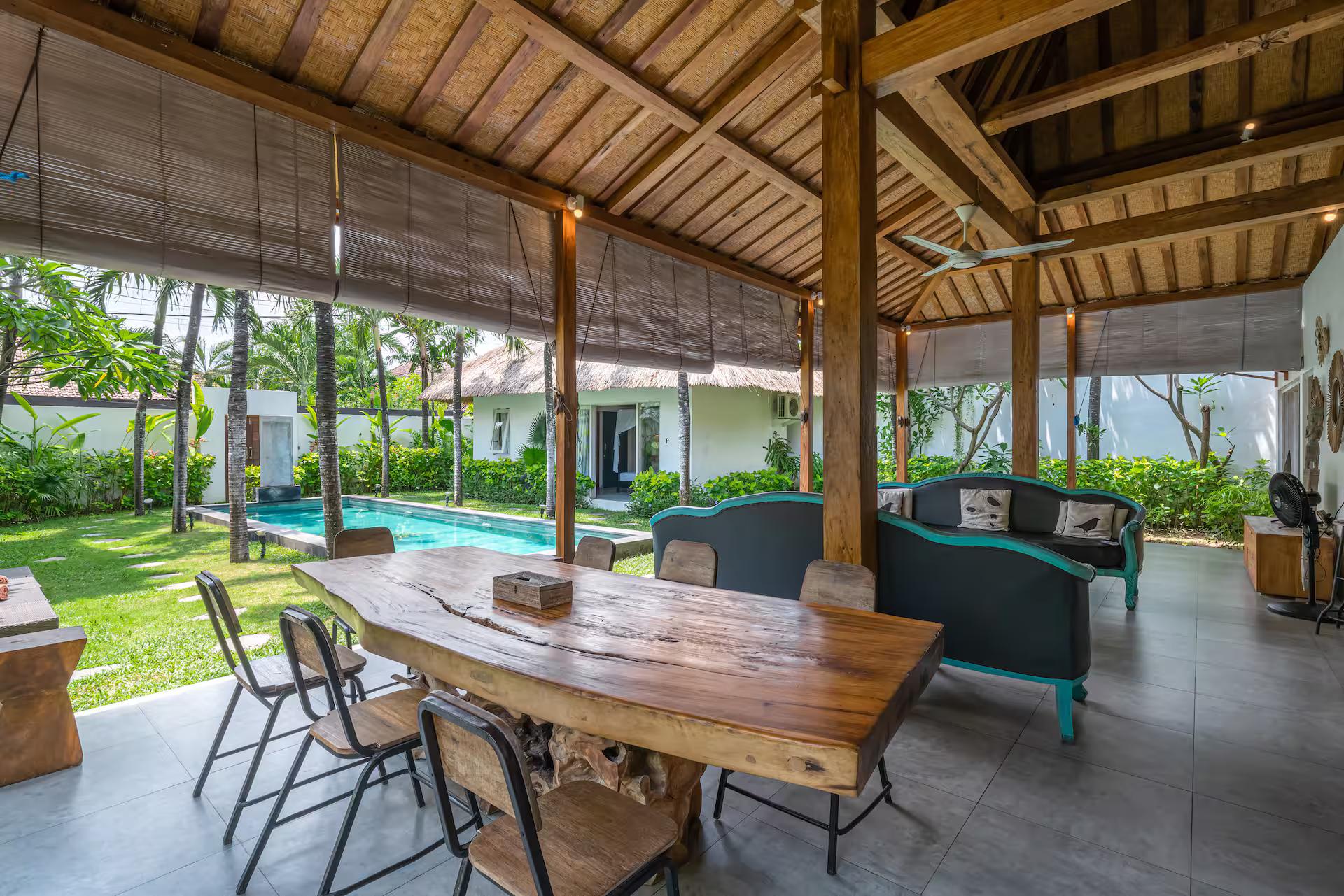 Long reclaimed-timber dining table in the open pavilion, lawn and pool beyond