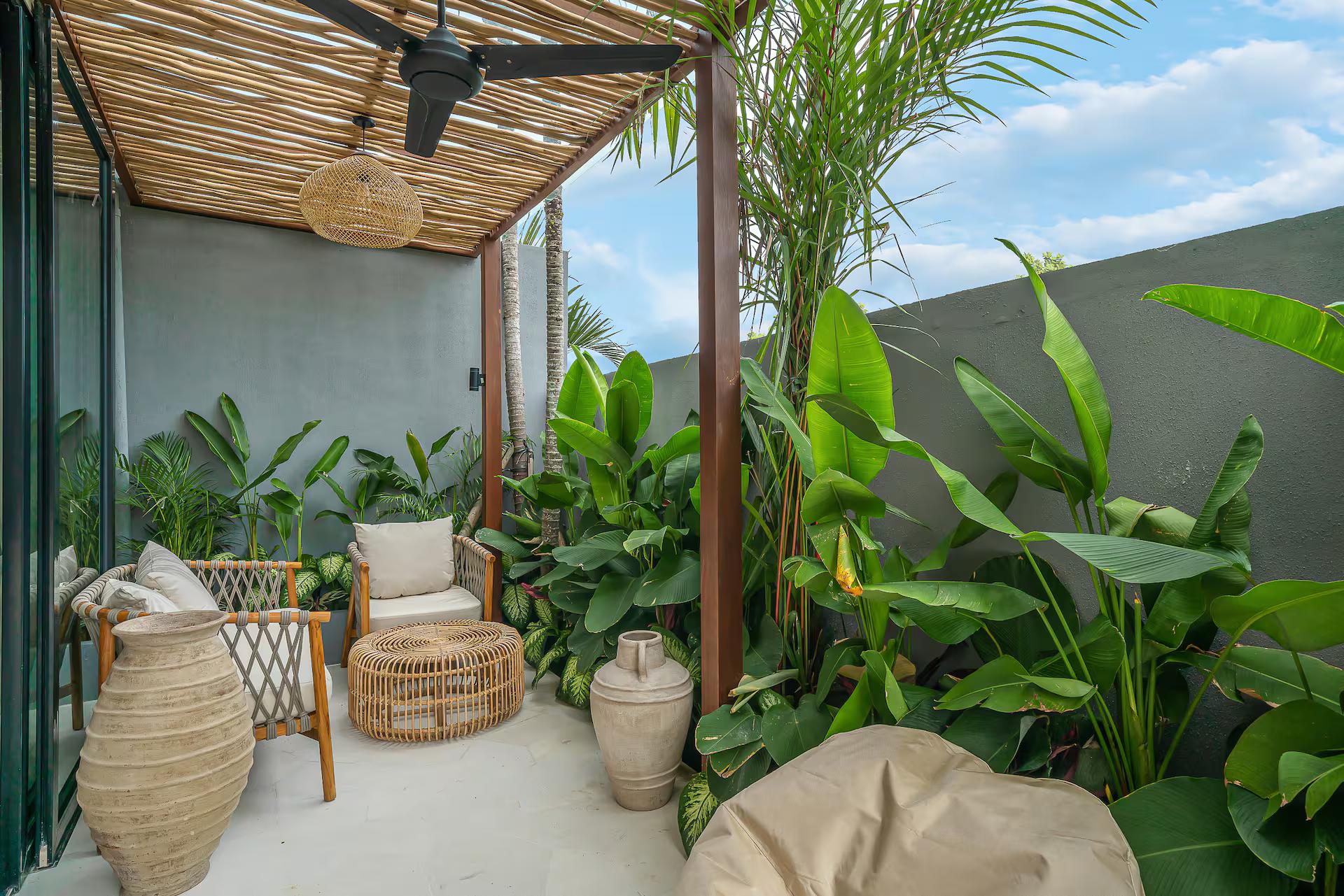 Cane chairs and terracotta urns in the side courtyard, shaded by a bamboo pergola and a ceiling fan