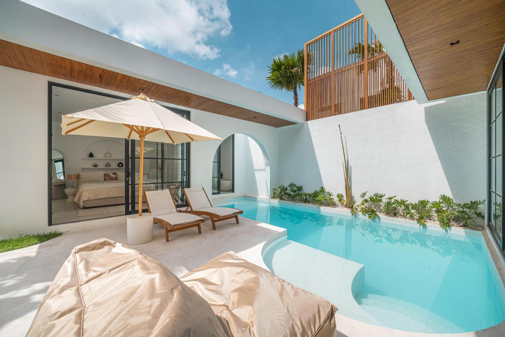Sun loungers and cushions on the pale stone deck beside the curved end of the pool