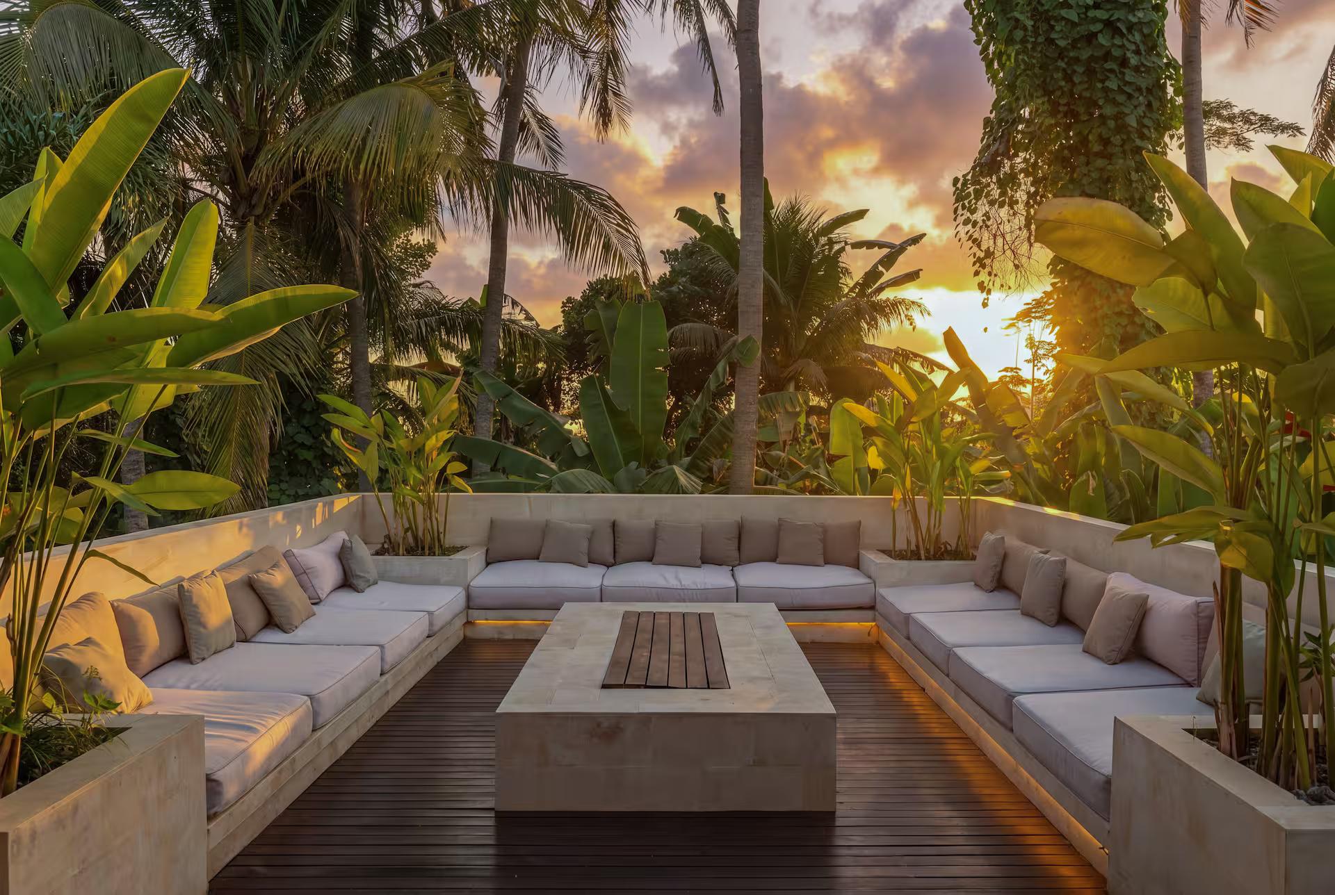 Sunset terrace with a U-shaped built-in lounge around a long timber table, jungle beyond