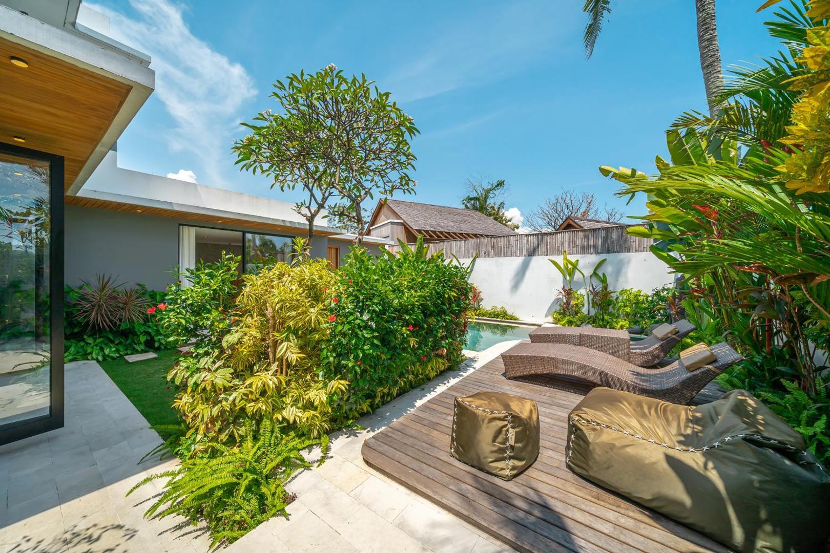 Raised timber deck and volcanic boulders beside the pool, banana palms crowding the wall