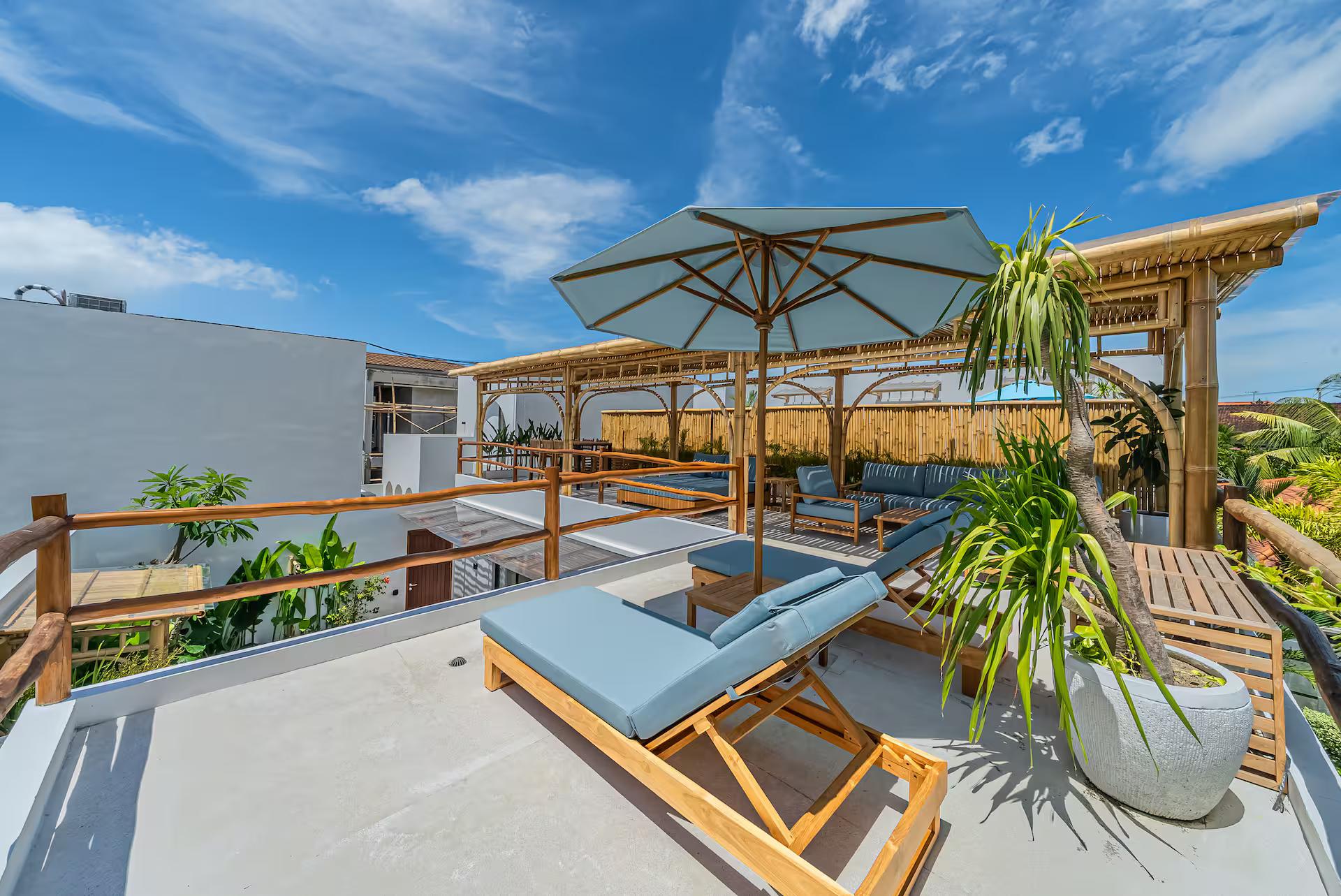 Sun loungers and a parasol on the bamboo rooftop terrace, village rooftops and rice fields beyond