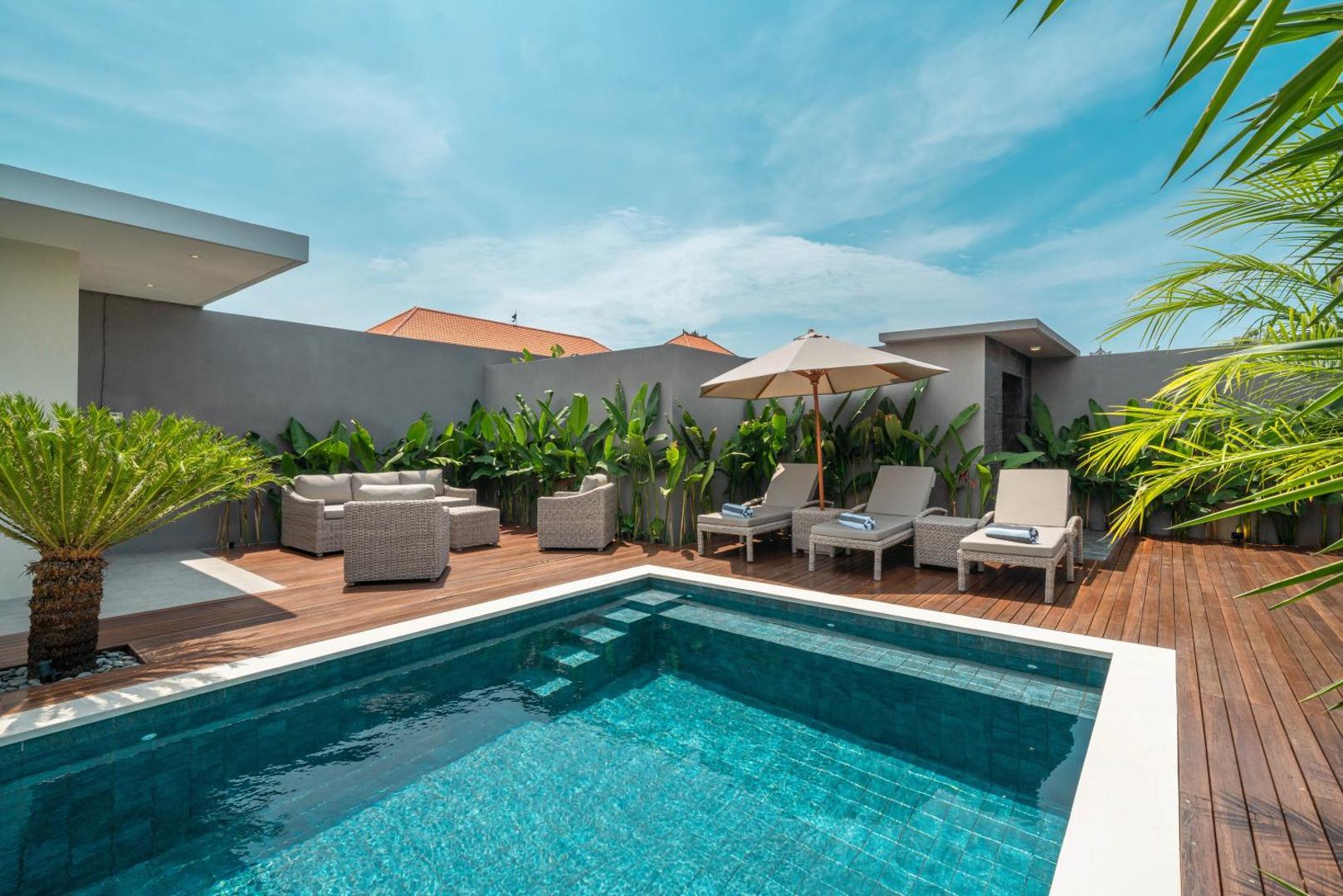 Sun loungers and a canvas parasol on the pool deck, planters of banana palm behind