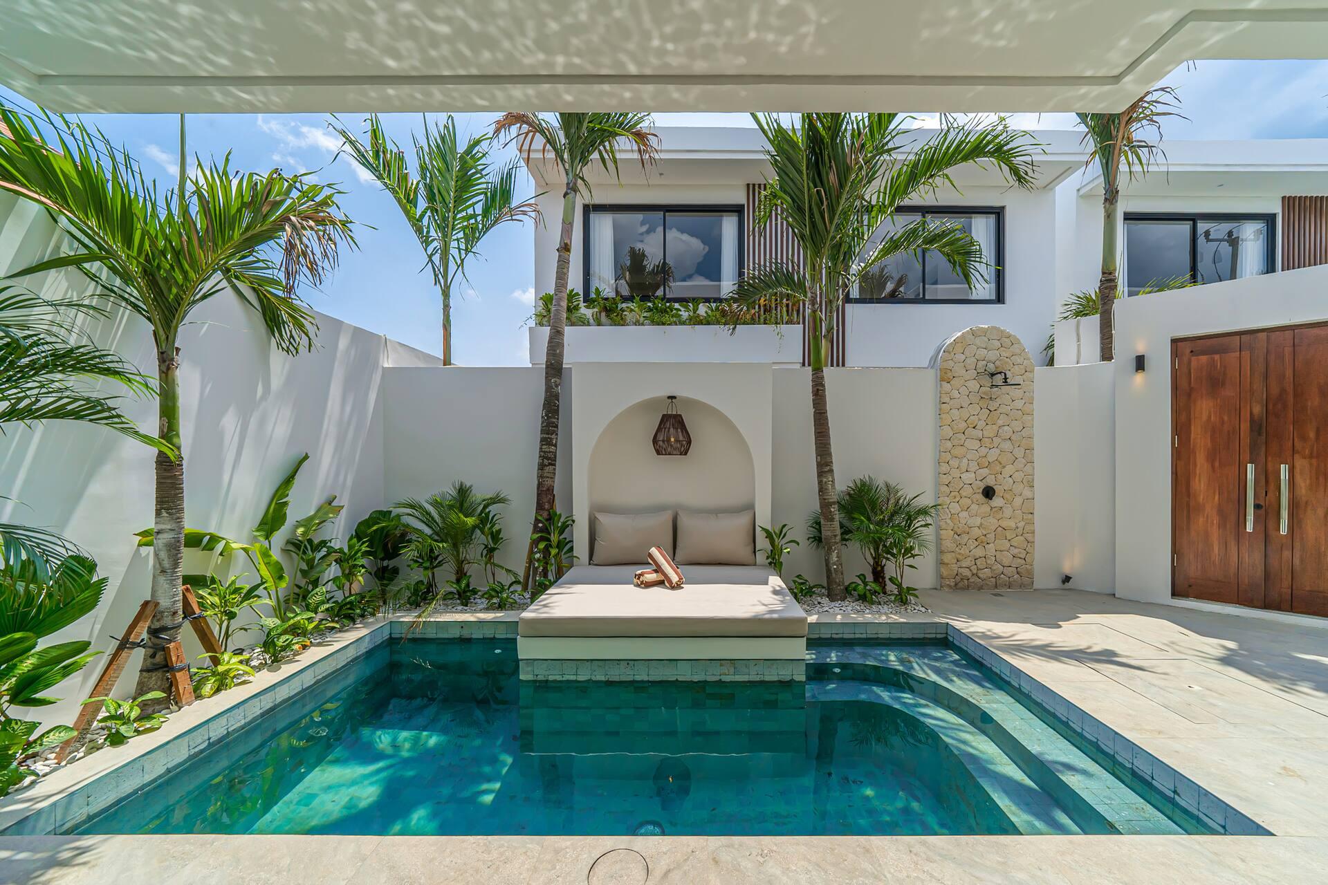 Cushioned daybed built out over the pool inside an arched alcove, palms overhead