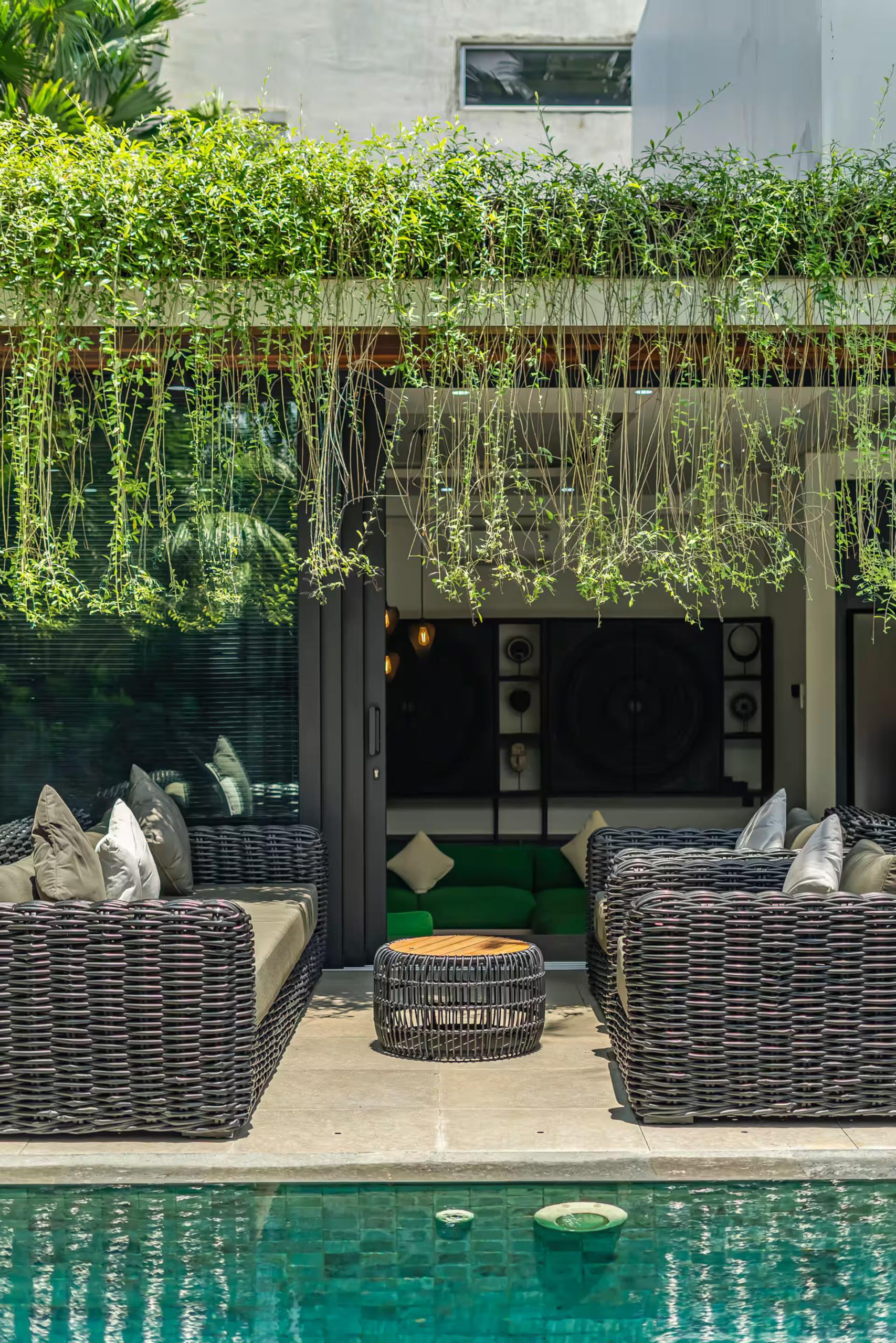 Rattan seating and outdoor speakers beneath a curtain of trailing greenery at the poolside