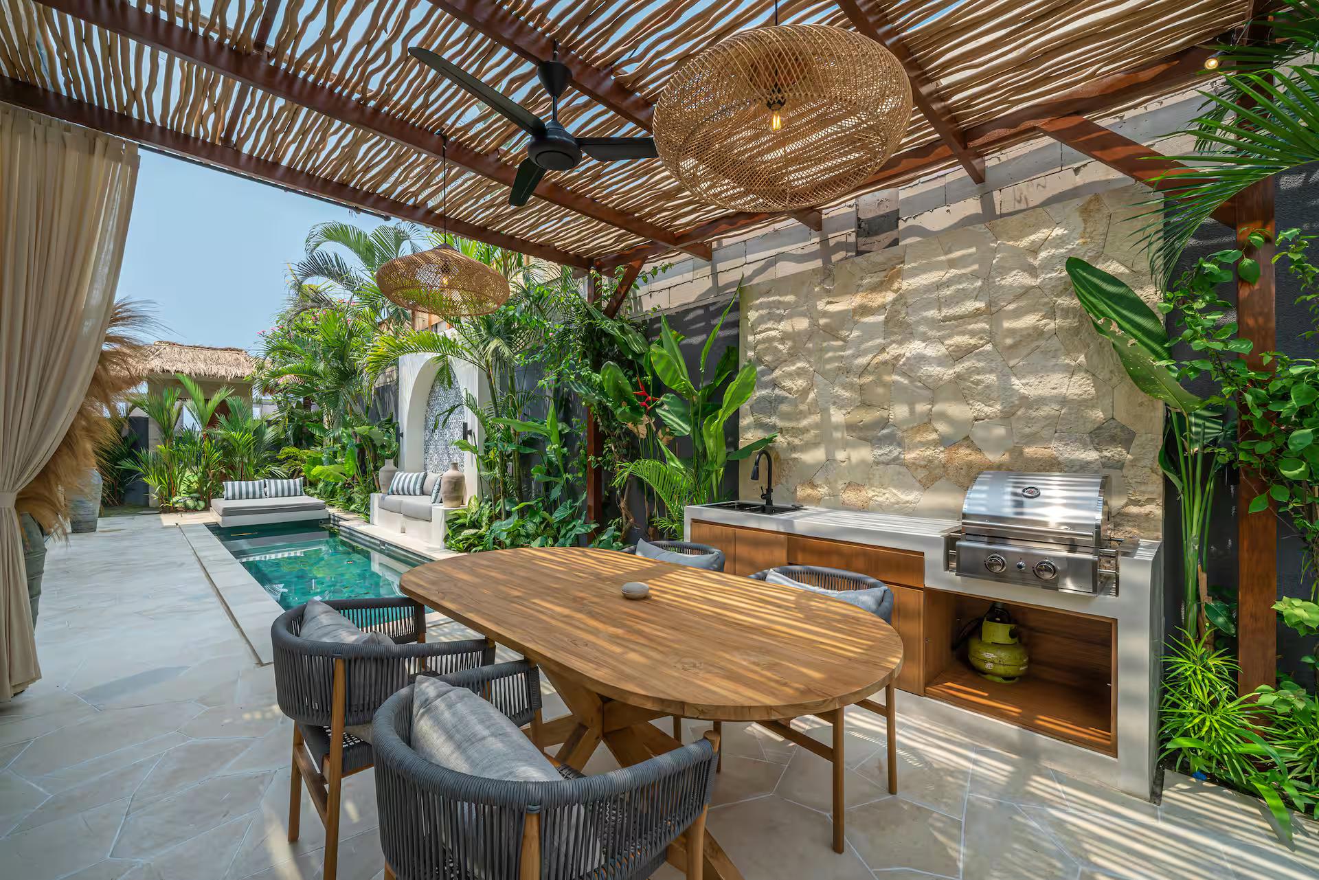 Reed-roofed pergola with an oval timber table and a barbecue built into stone
