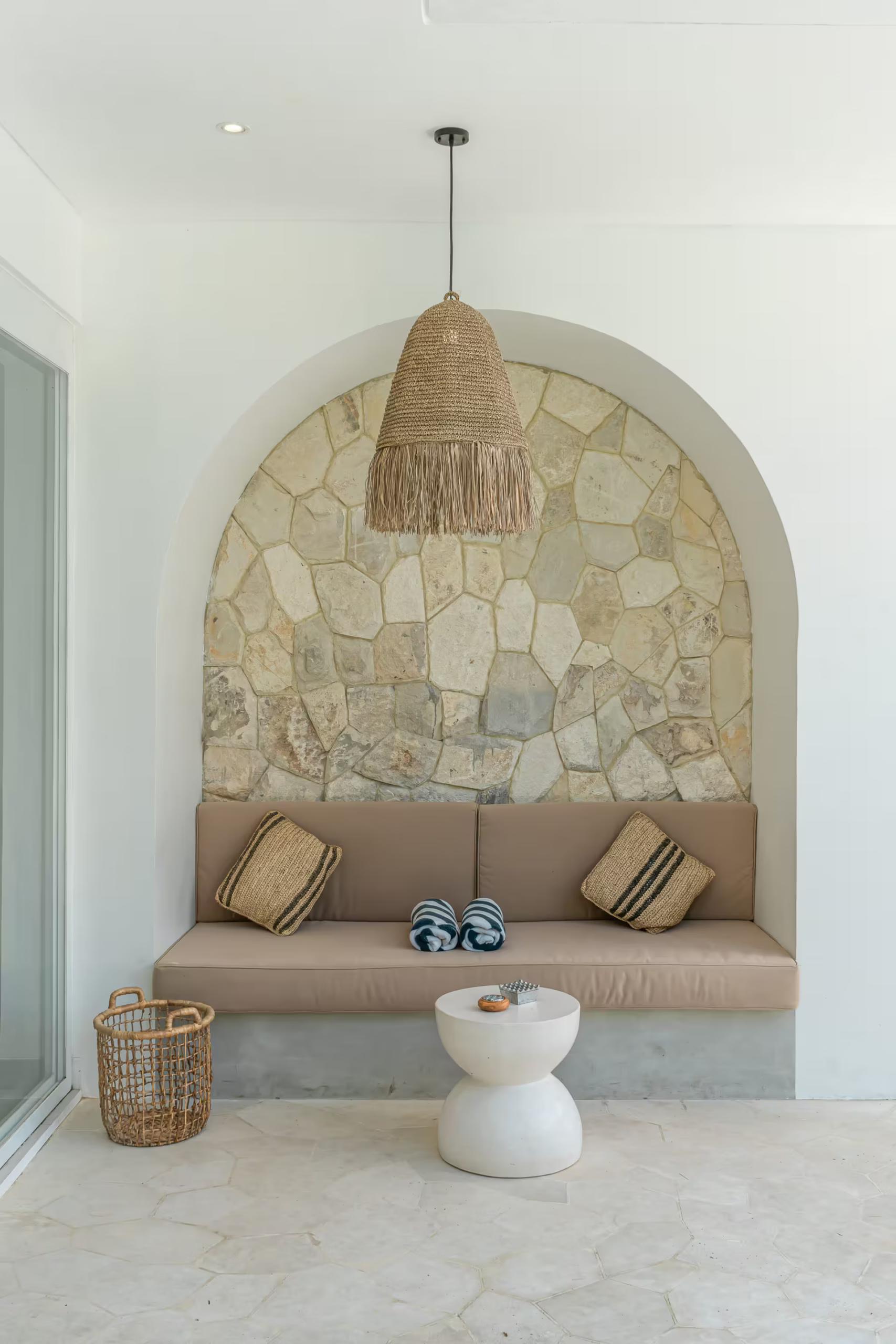Stone-clad arched alcove with a long built-in banquette and a fringed rattan pendant