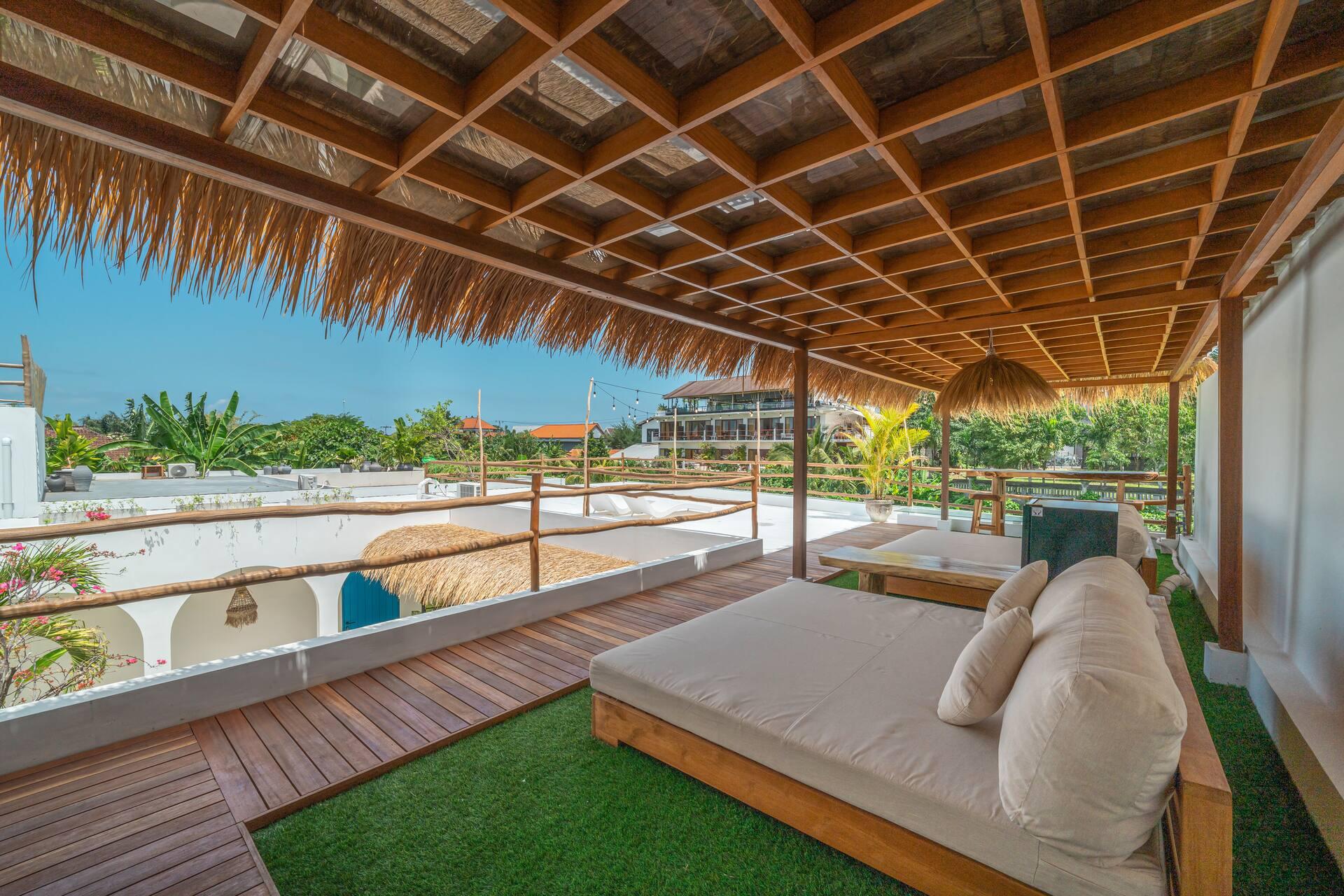 Teak daybed on the rooftop sundeck under thatch, gardens and rooftops beyond the rail