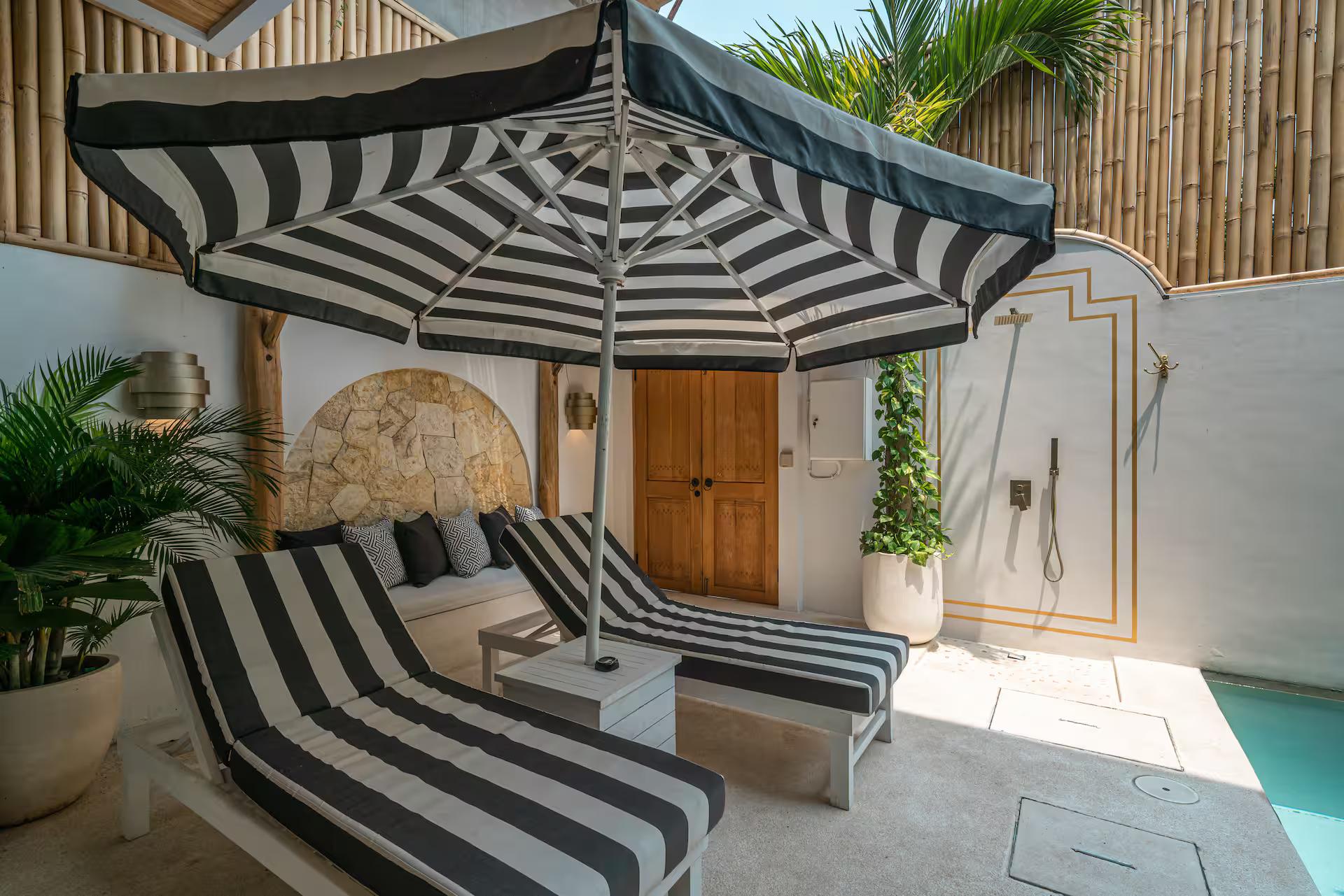 Black-and-white striped daybed and lounger beside an arched stone niche and brass outdoor shower