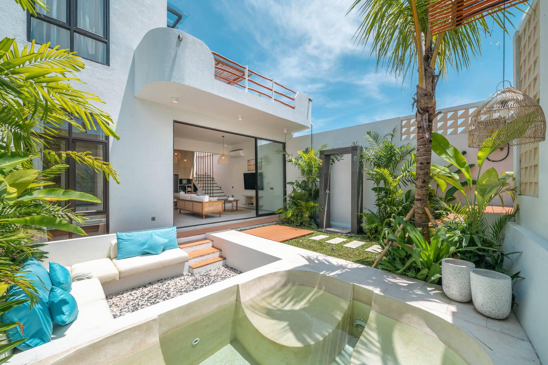 Turquoise cushions on the built-in poolside bench, with palms and heliconia around the courtyard