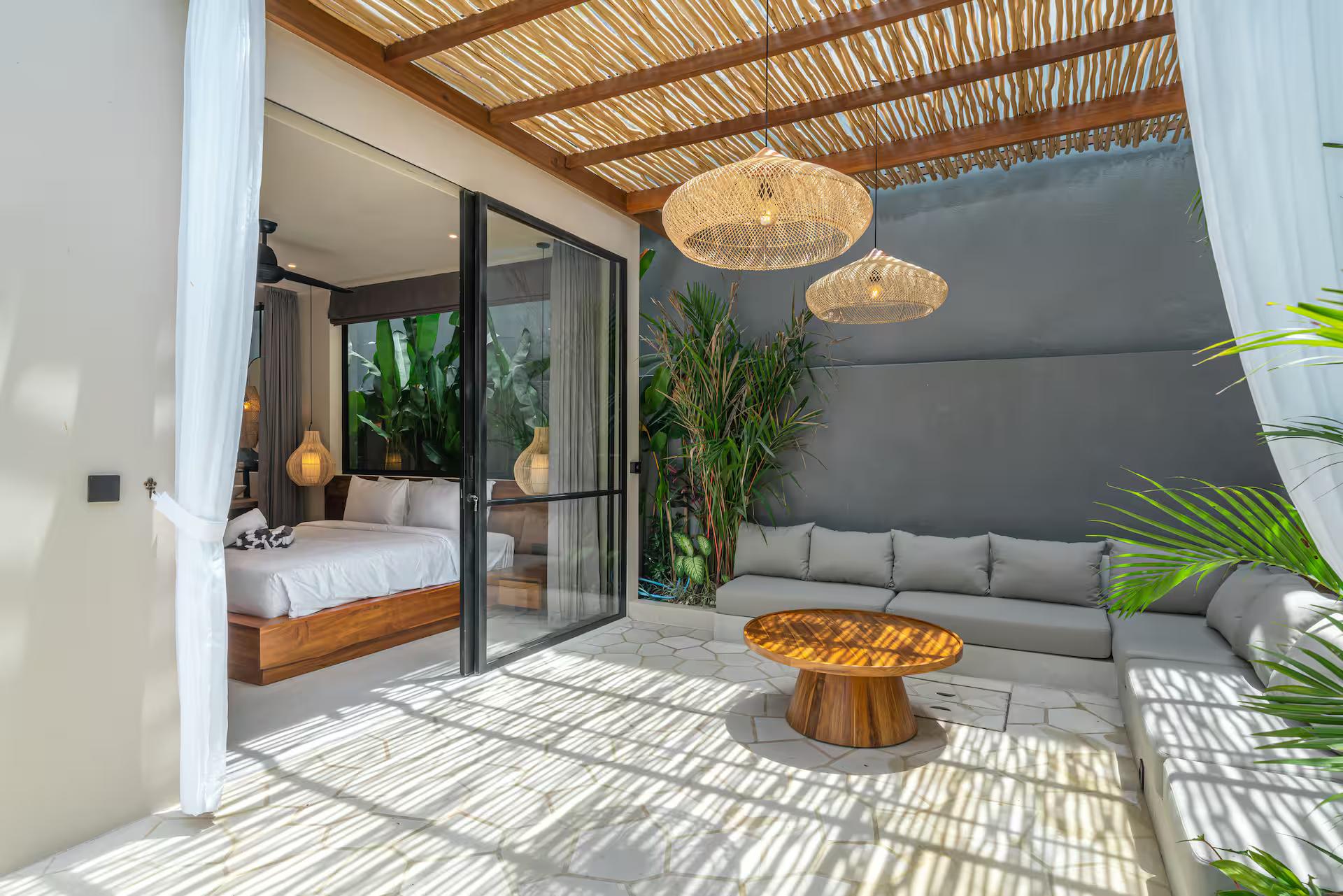 Covered outdoor lounge beneath an alang-alang ceiling, low sofa and round timber table