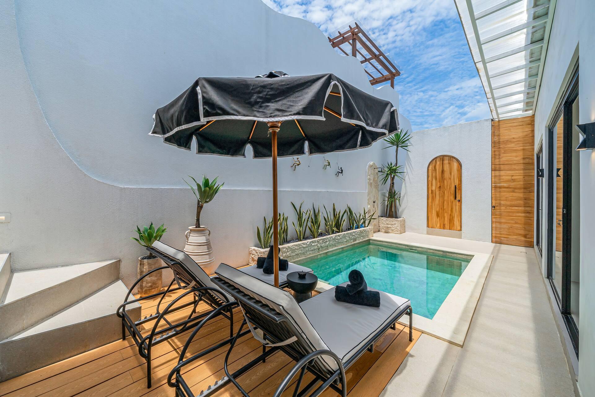 Black-framed loungers and a parasol on the timber deck beside the courtyard pool