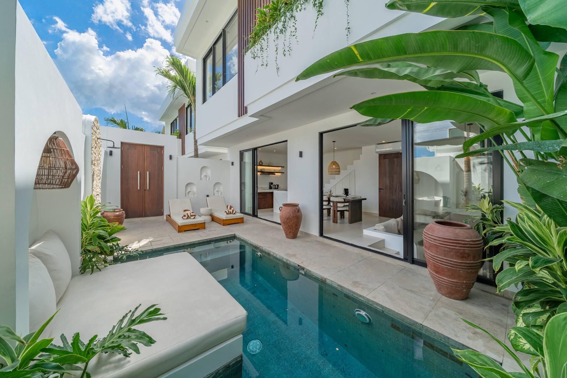 Turquoise water and a terracotta urn beside the glazed living room of Nova Oasis Berawa 2, framed by traveller's palms