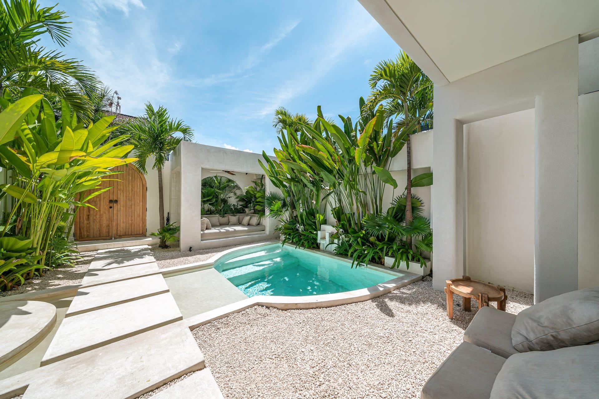 Freeform pool beside a gravel sun terrace, framed by banana plants and palms under a clear Pererenan sky