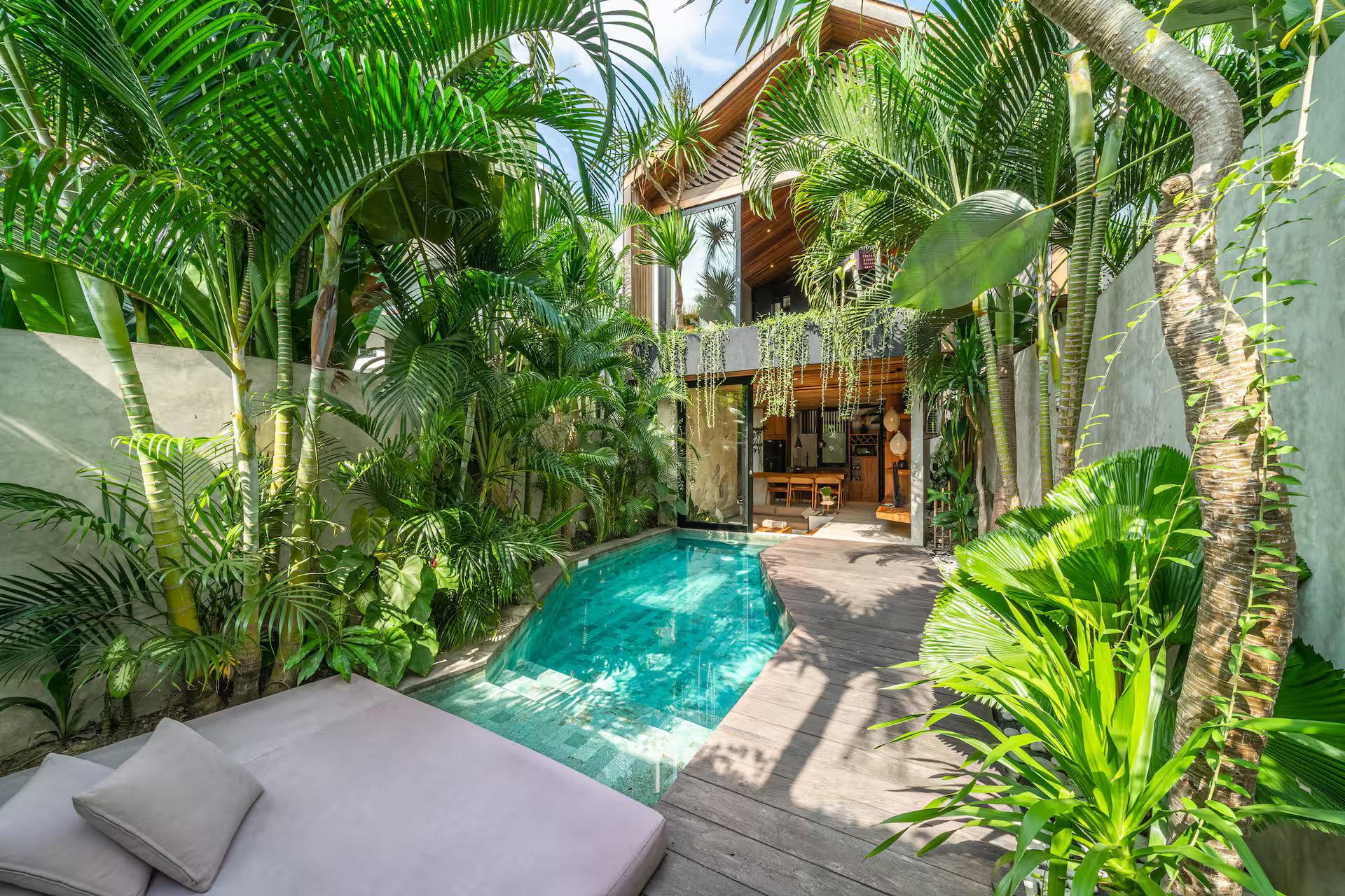 Low daybed in the shade at the far end of the pool, banana leaf and areca palm overhead