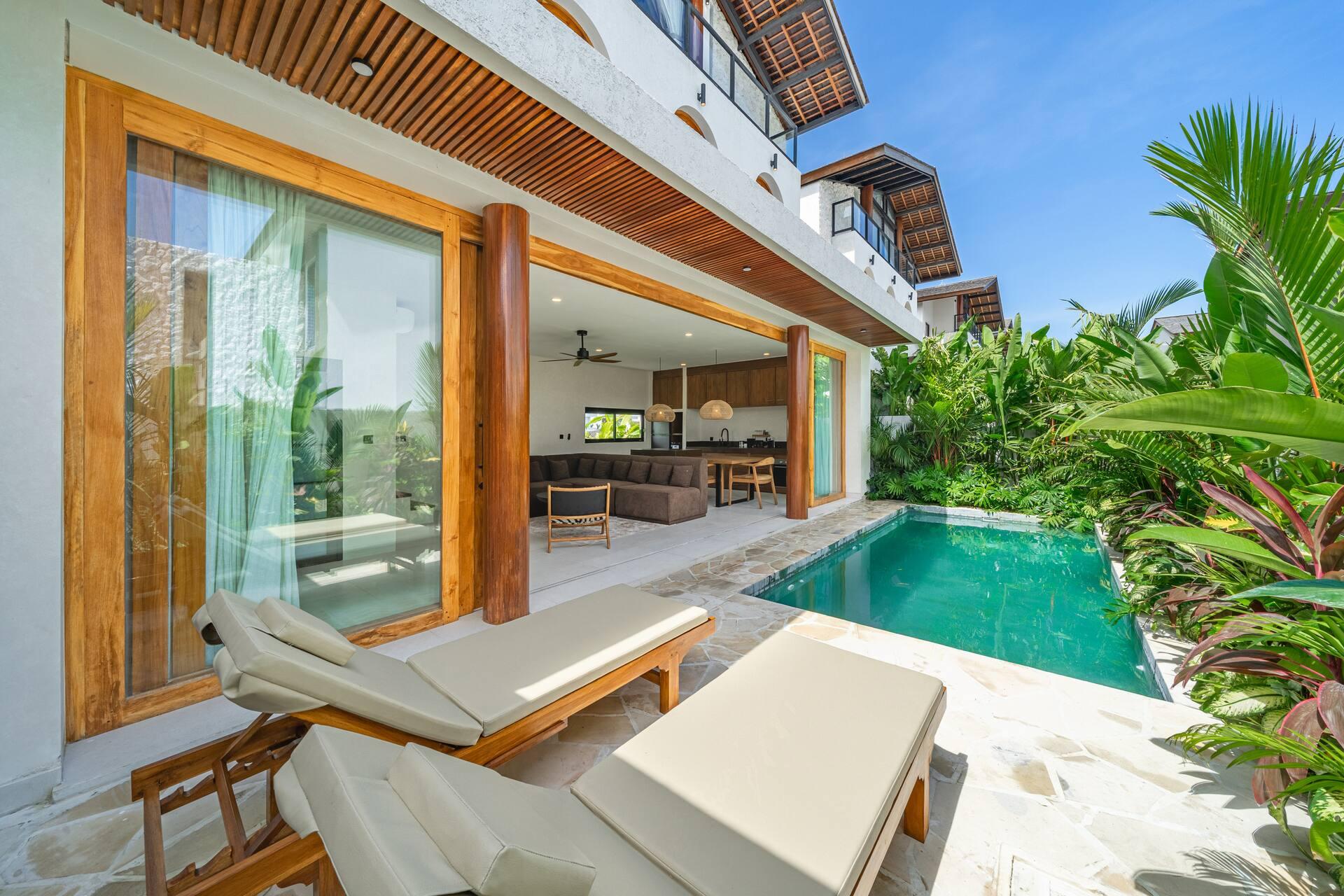 Two timber sun loungers on the flagstone deck beside the pool, glass doors folded open behind