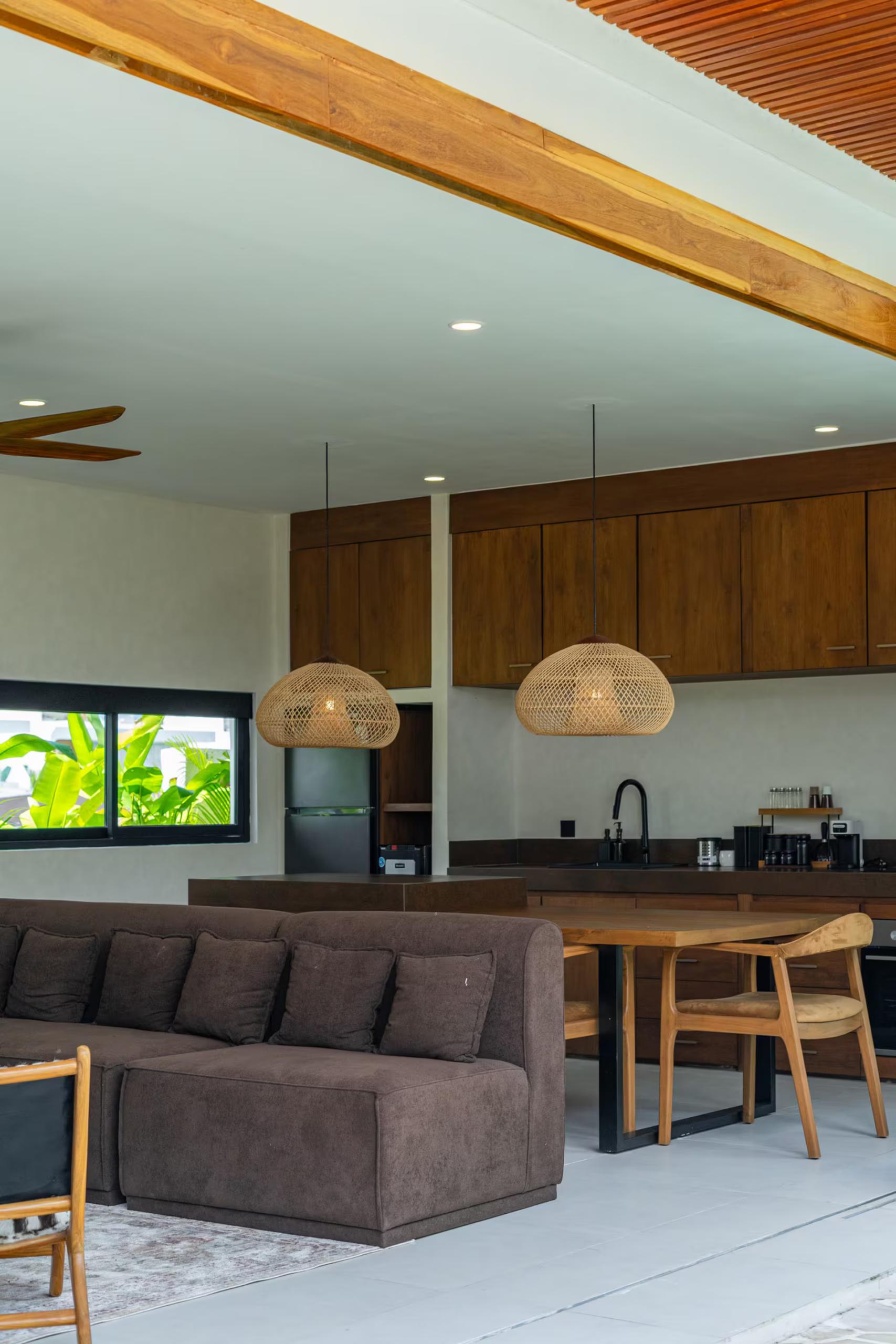 Open-plan living and kitchen at Villa Terra Calma, teak cabinetry under two woven rattan pendants