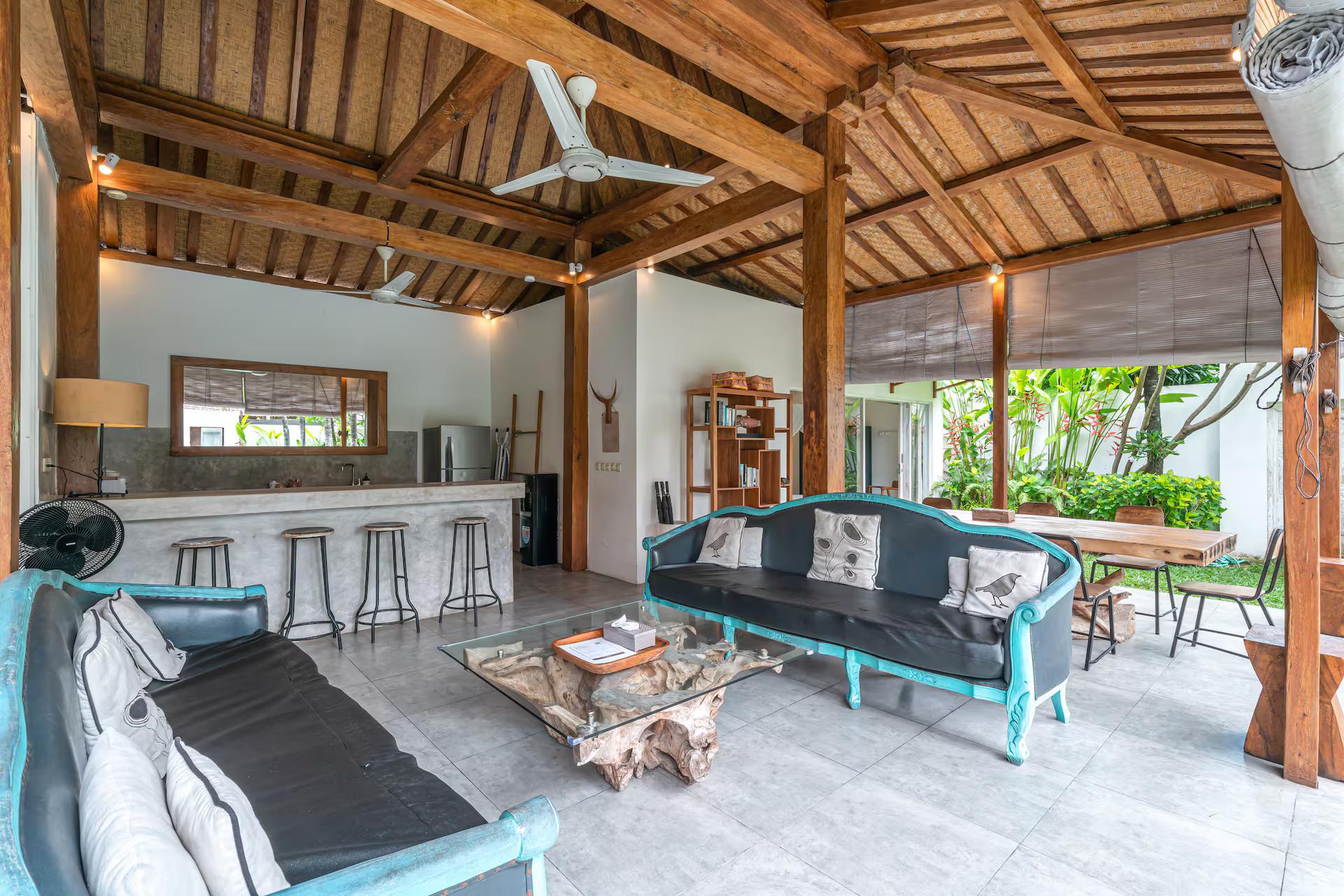Open-sided living pavilion with teal daybeds under a bamboo and alang-alang ceiling