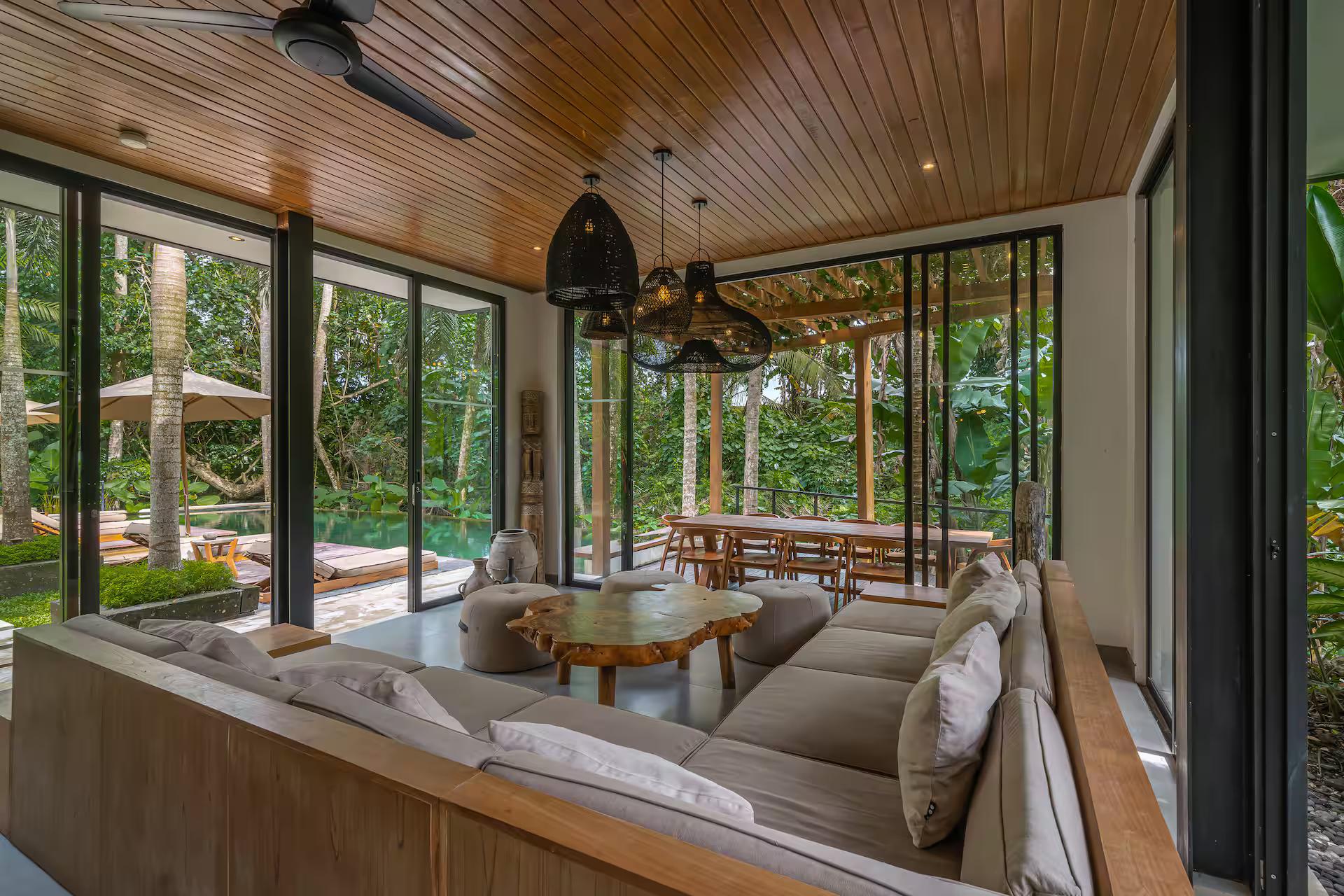 Living room at Villa Yuka under a slatted timber ceiling, glass walls open to the pool