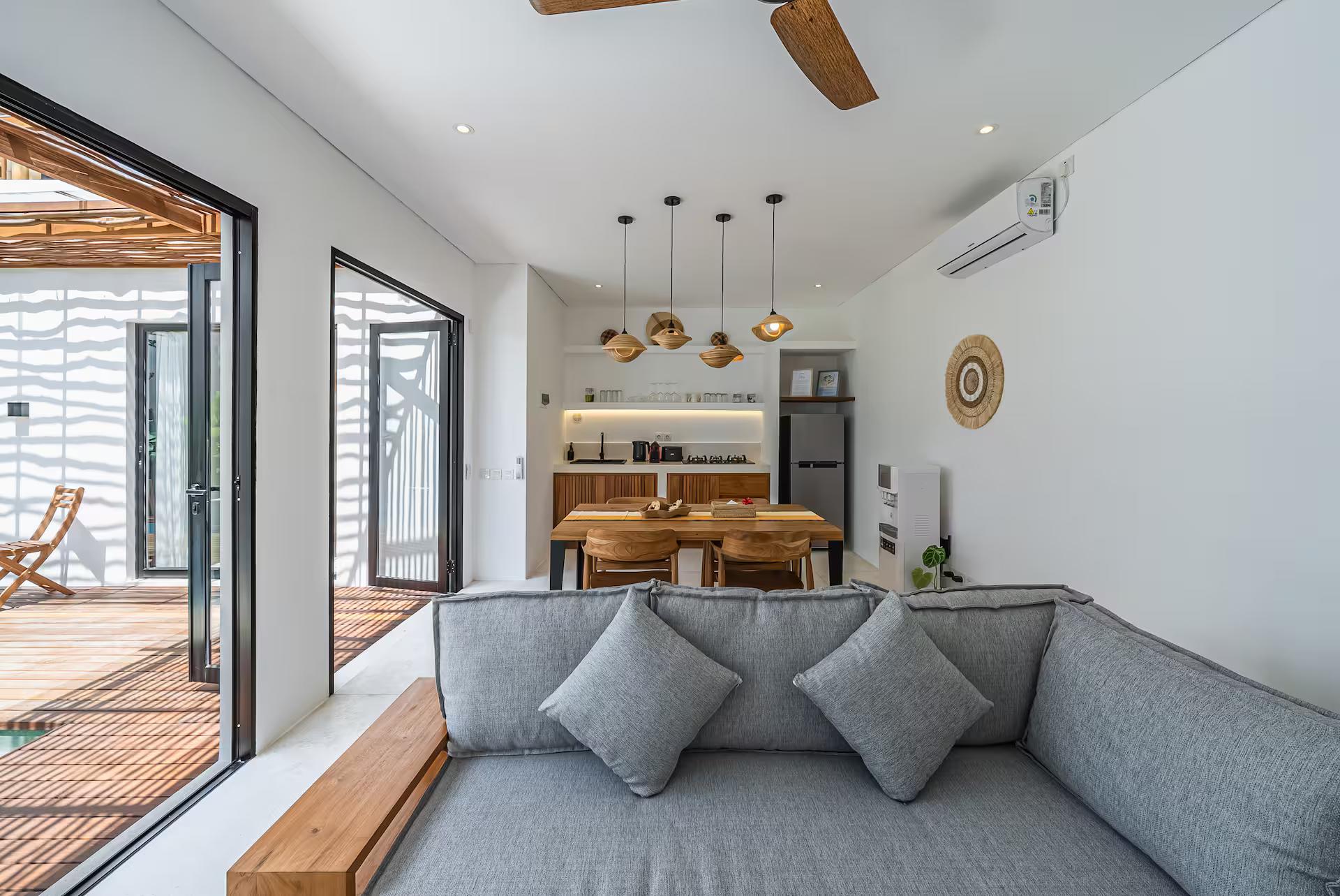 Open-plan lounge with a deep grey sofa, sliding glass folded back onto the pool deck