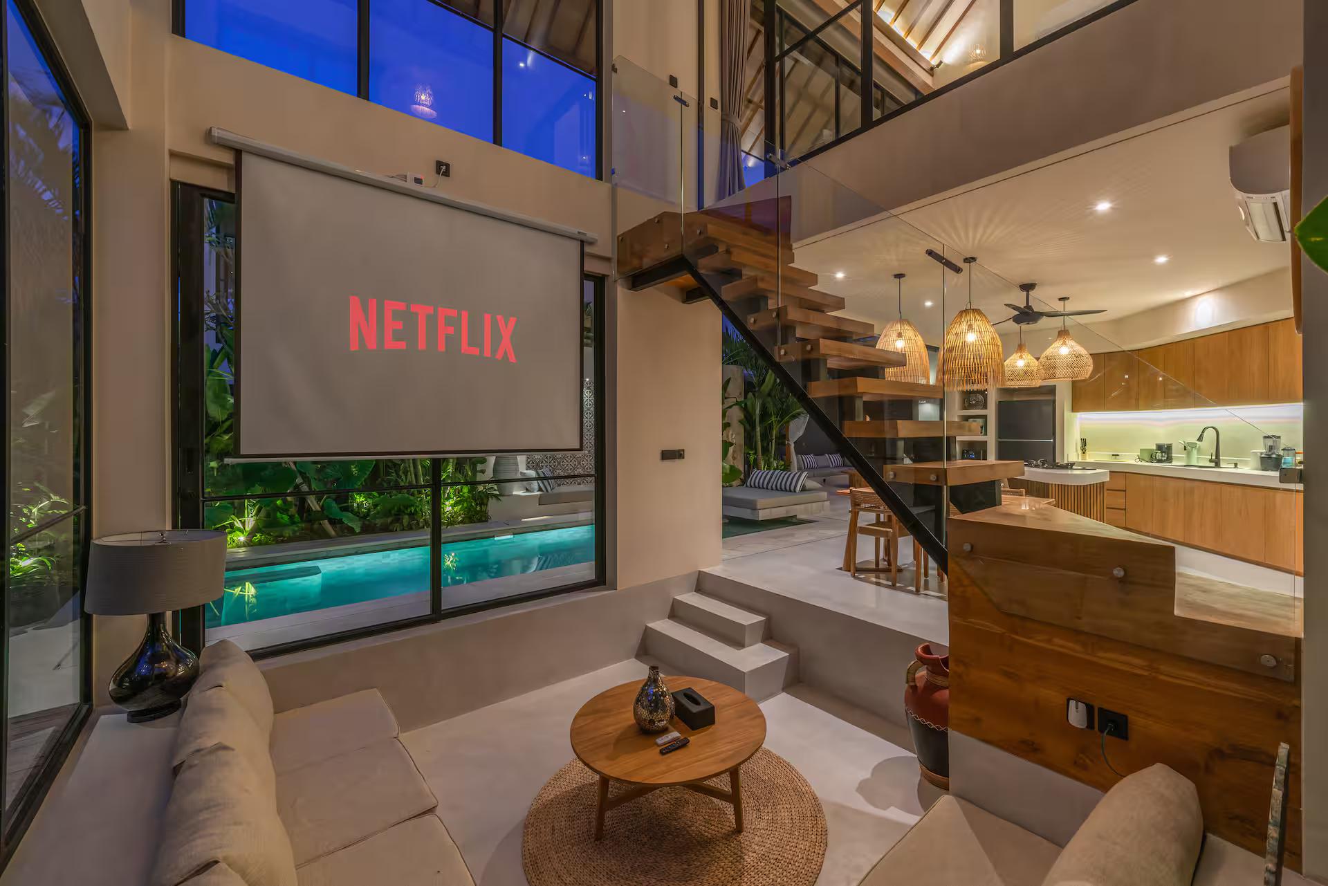 Double-height living room at Villa Nalaka, projector screen beside the black steel staircase