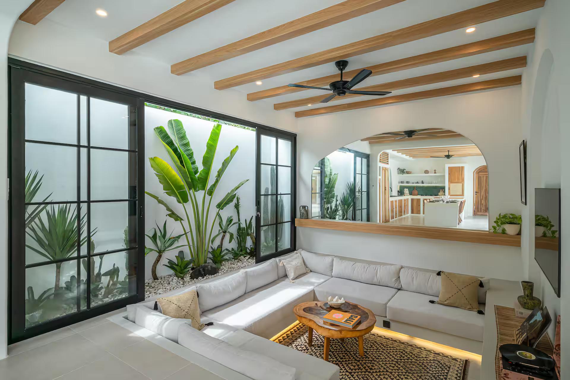Low white sectional under exposed timber beams, black steel windows onto the planting