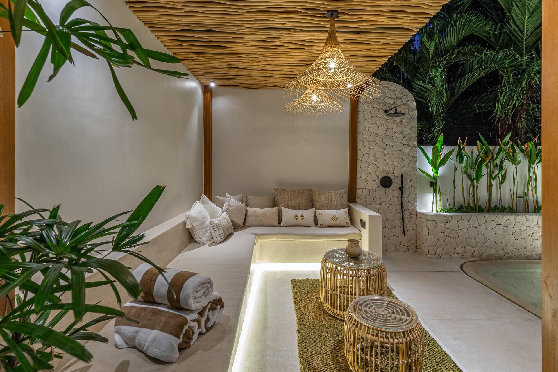 A built-in banquette lounge under a thatched pergola beside the pool, dressed with woven cushions