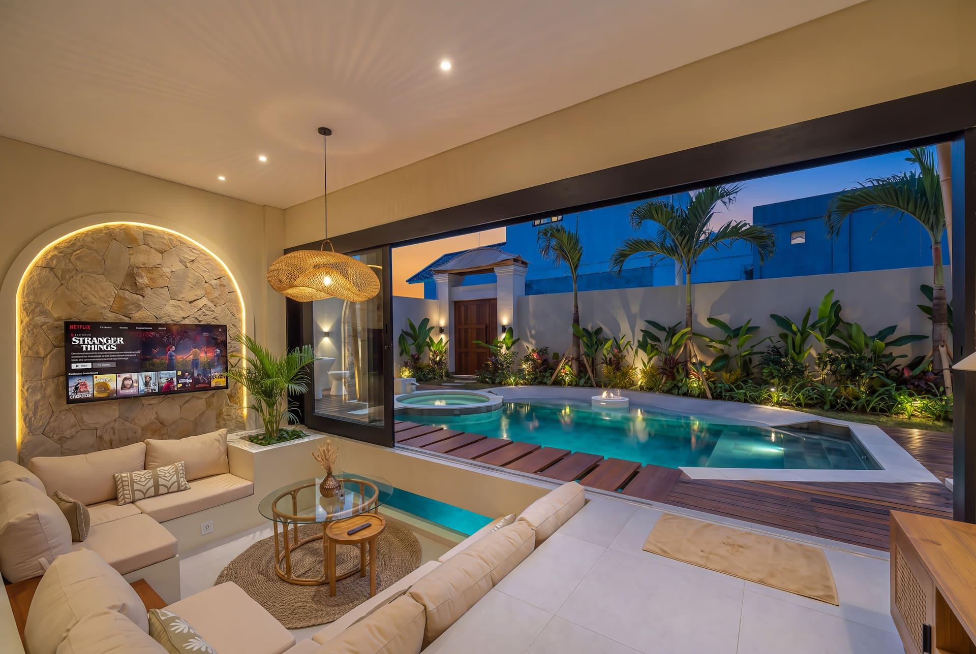 Living room at Villa Tigana opening through a full wall of glass to the lit pool at dusk