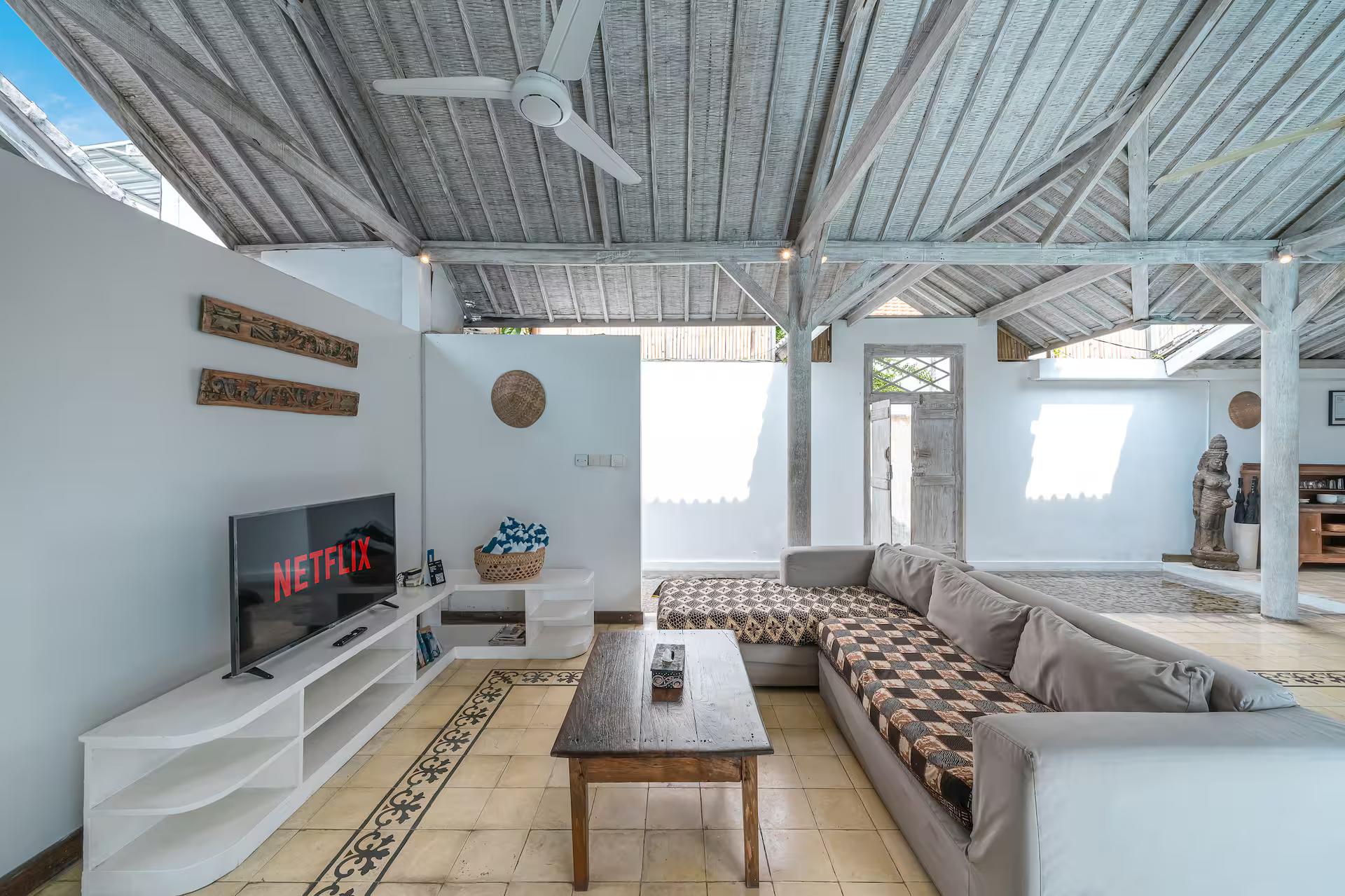 Open-sided living pavilion with batik-cushioned sofas, a smart TV and patterned cement tile