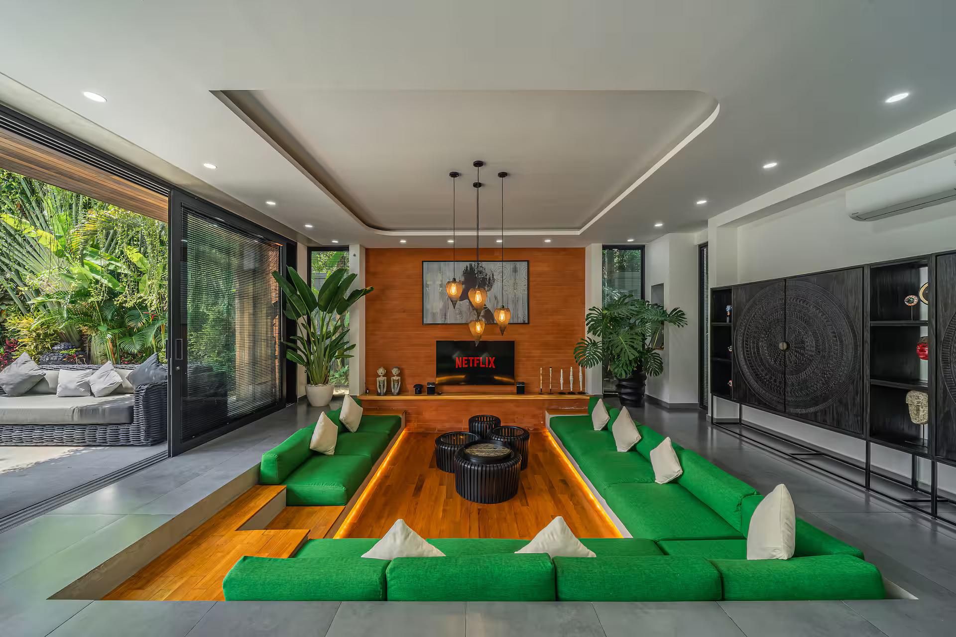 Sunken lounge of emerald cushions set into a timber-lined pit facing a large screen