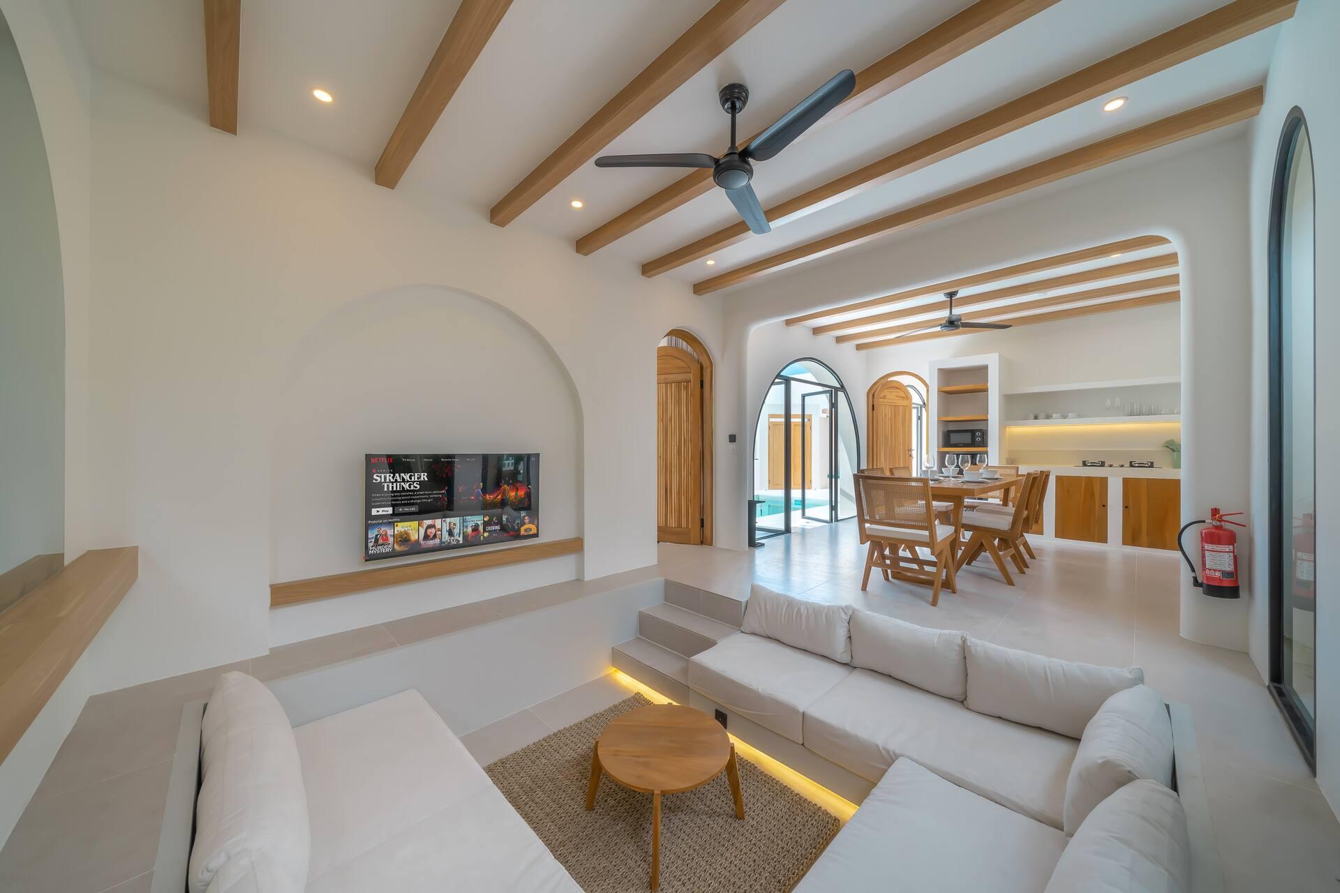 Open-plan living room at Villa Sorrento, a long built-in sofa beneath pale timber ceiling beams