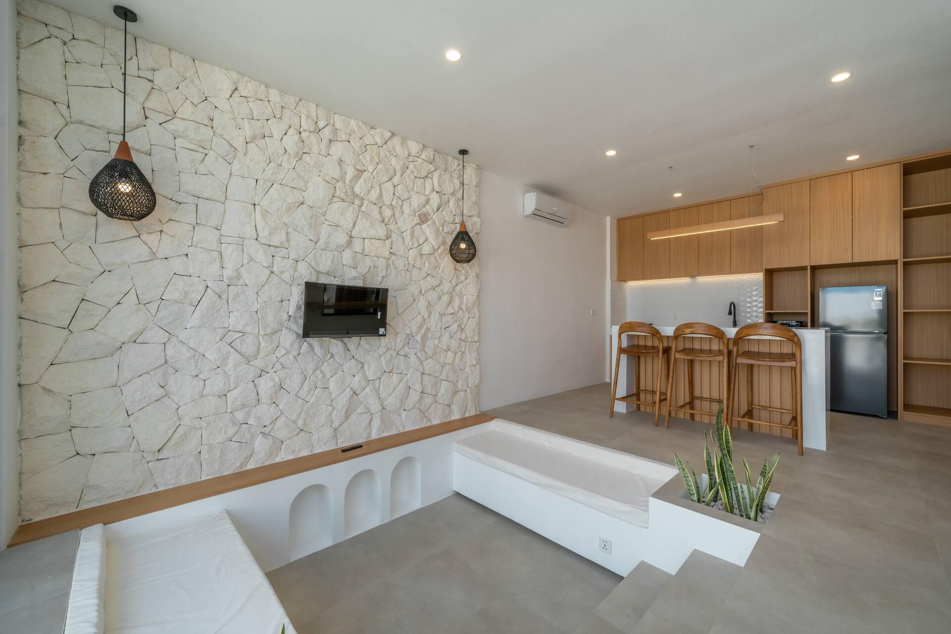 Sunken lounge with built-in white bench seating beneath a rough-cut stone feature wall and woven pendants