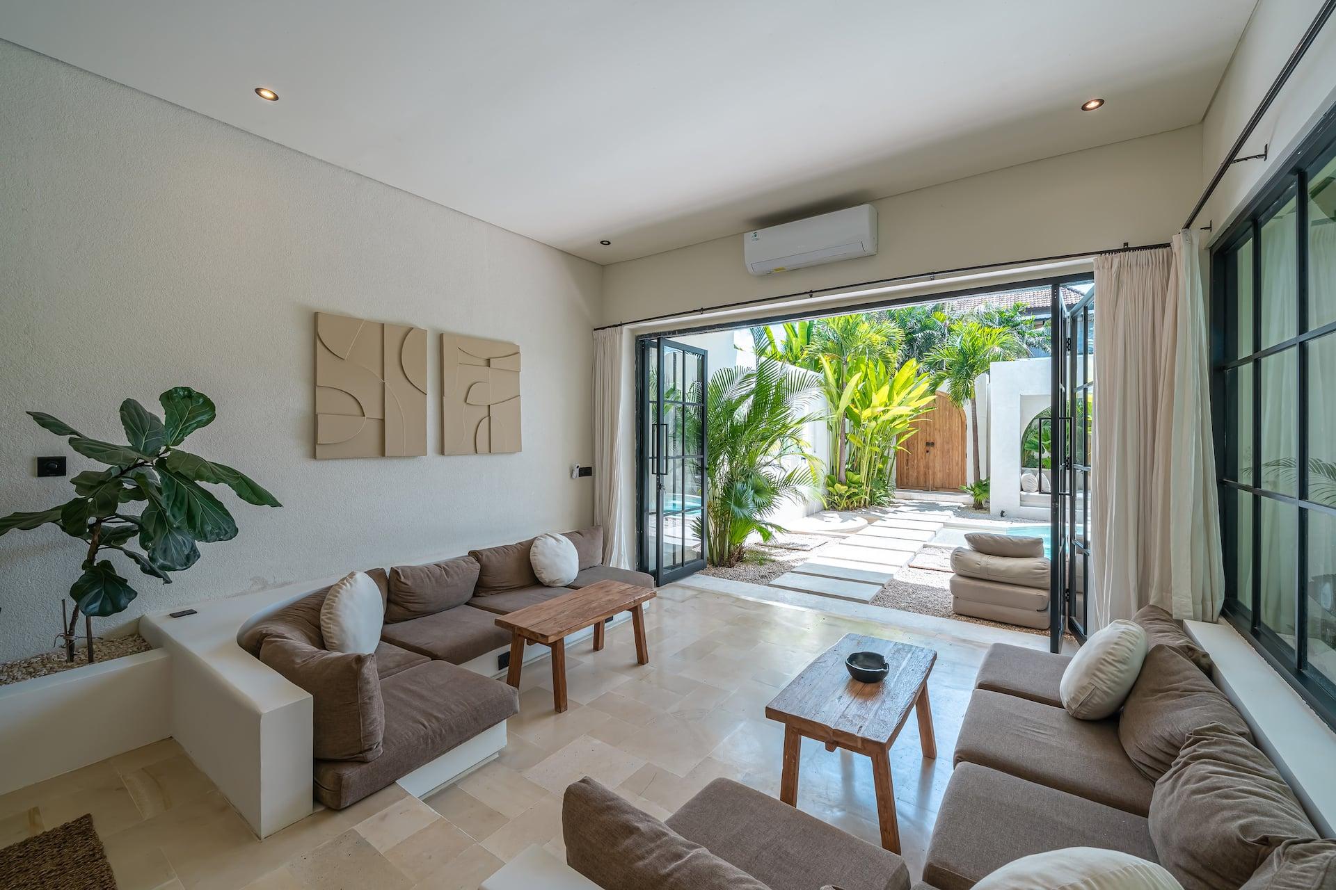 Sunken living room with cushioned built-in banquettes and timber tables, opening onto the pool through steel-framed doors