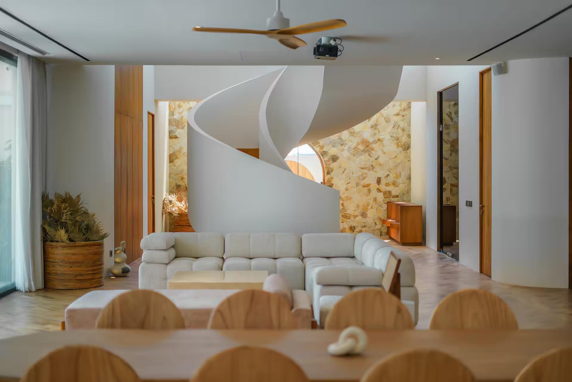 The living room at Villa Babylon, bouclé sofas gathered beneath a sculptural spiral staircase