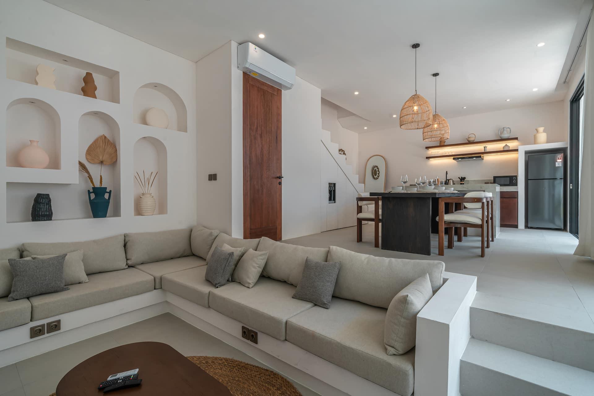 Sunken living room with an L-shaped linen banquette, arched display niches and rattan pendants