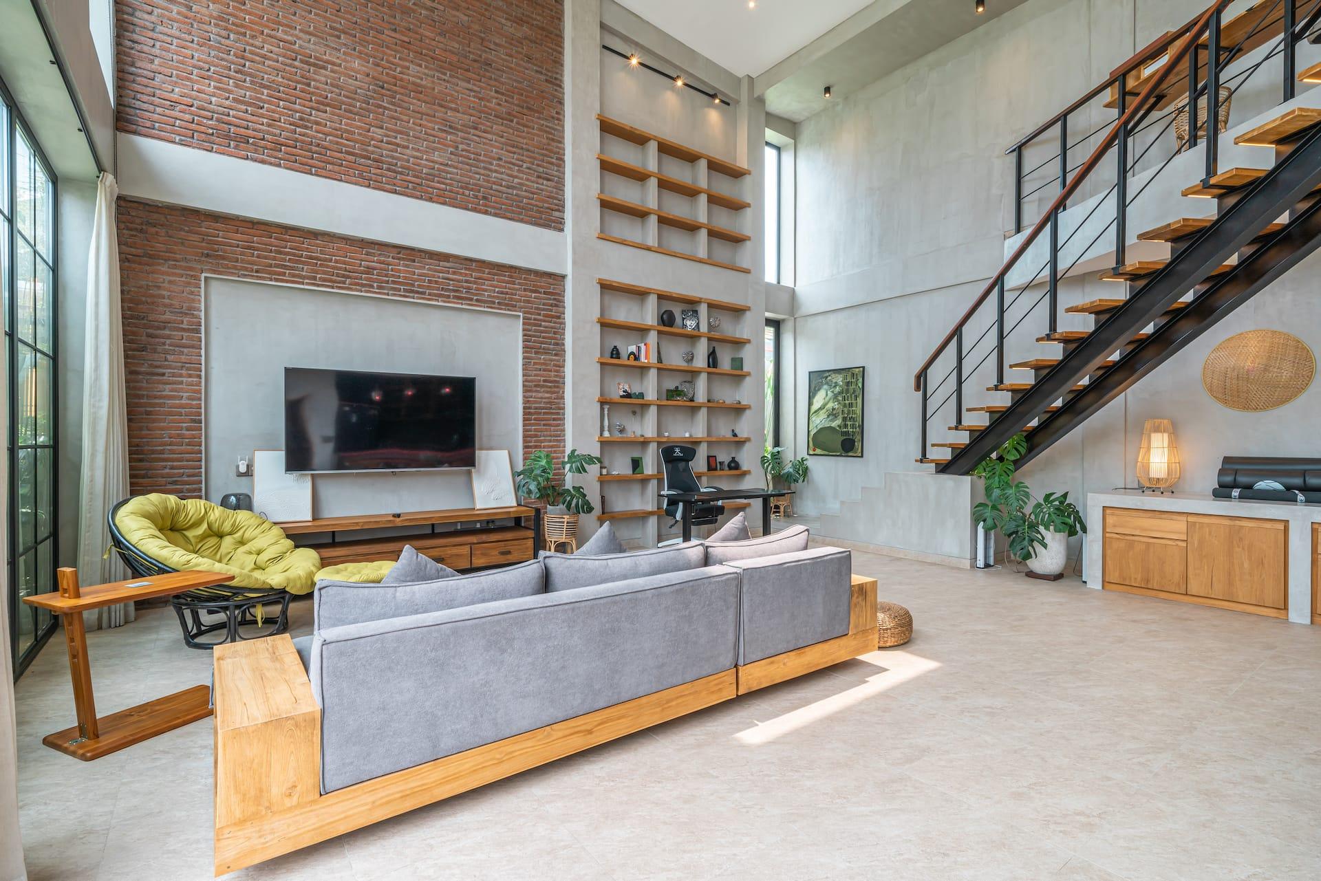 Double-height living room with an exposed brick wall, grey sectional sofa and steel staircase