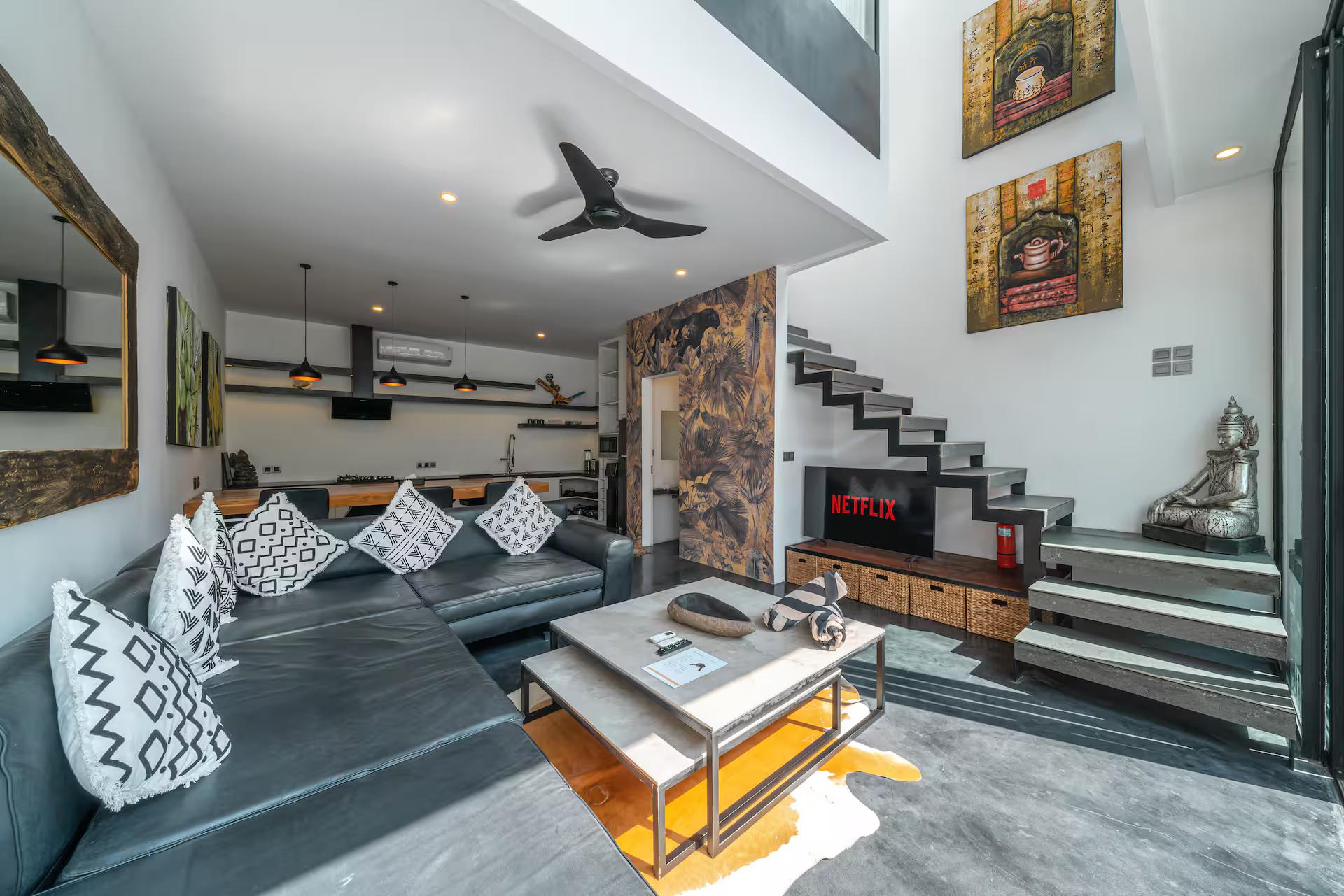 Double-height living room with a grey sectional and the concrete stair behind