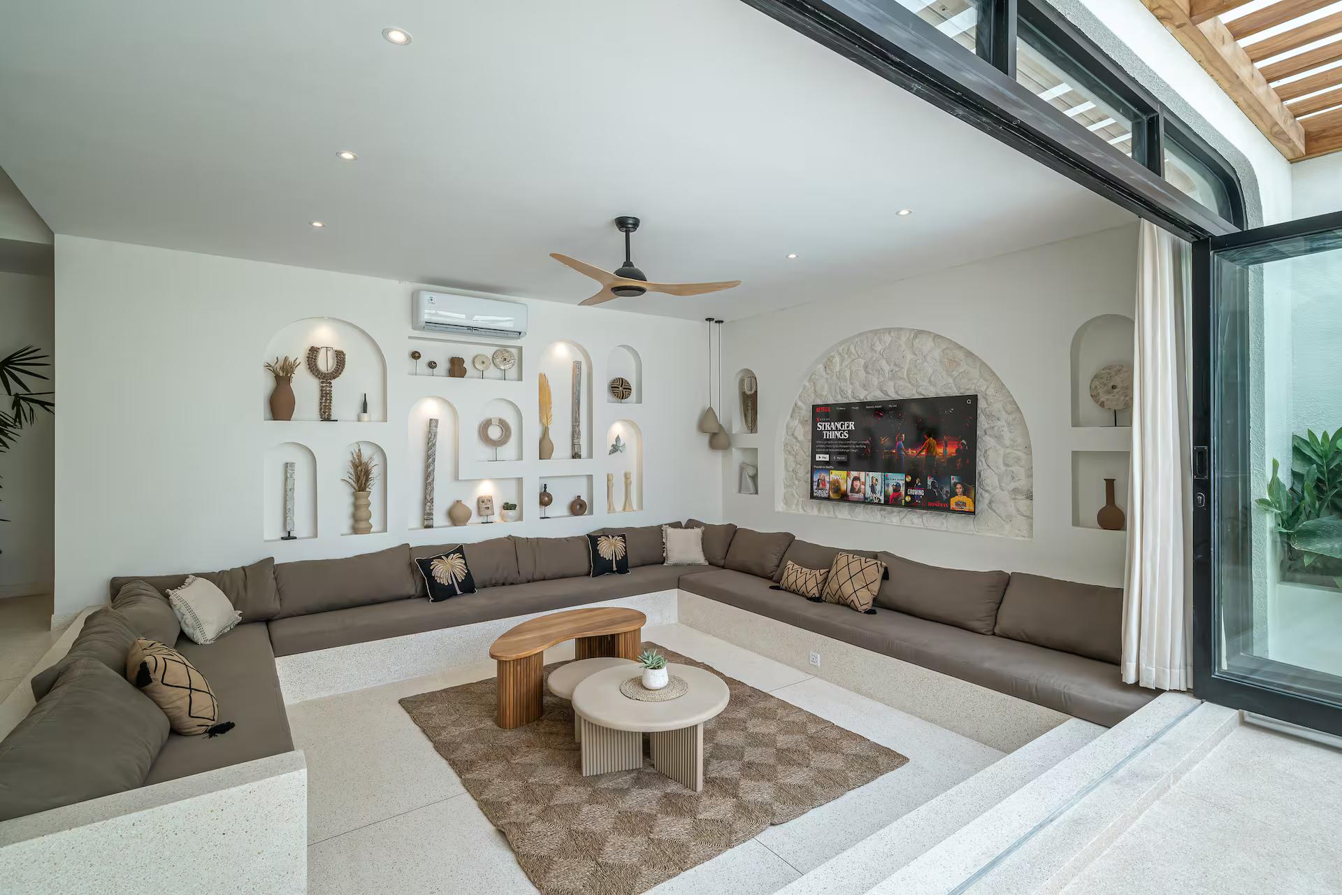Sunken lounge with a low sectional beneath a wall of arched display niches, open to the pool