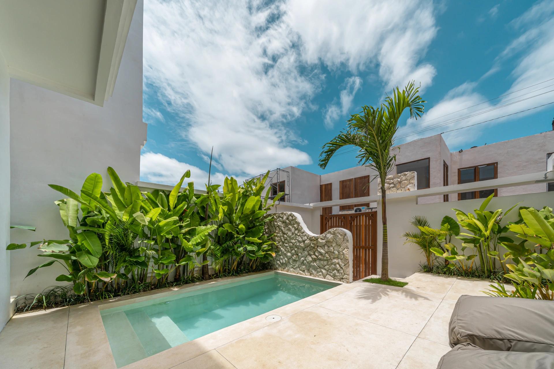 Banana and heliconia along the pool wall at Villa Kembali 10, a teak gate set into the stone